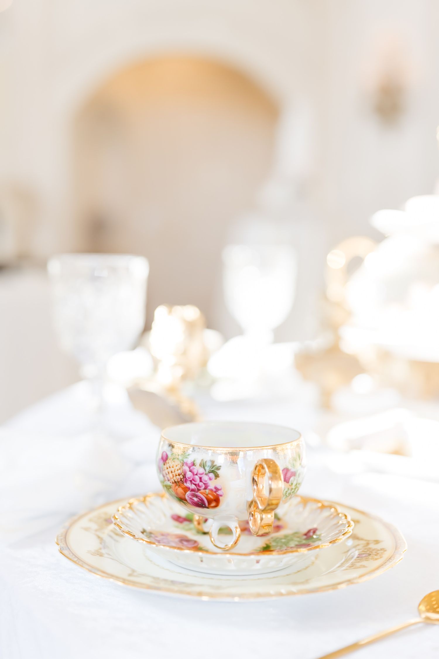 Vintage floral teacups with gold trim and delicate butterfly patterns arranged on white linens.