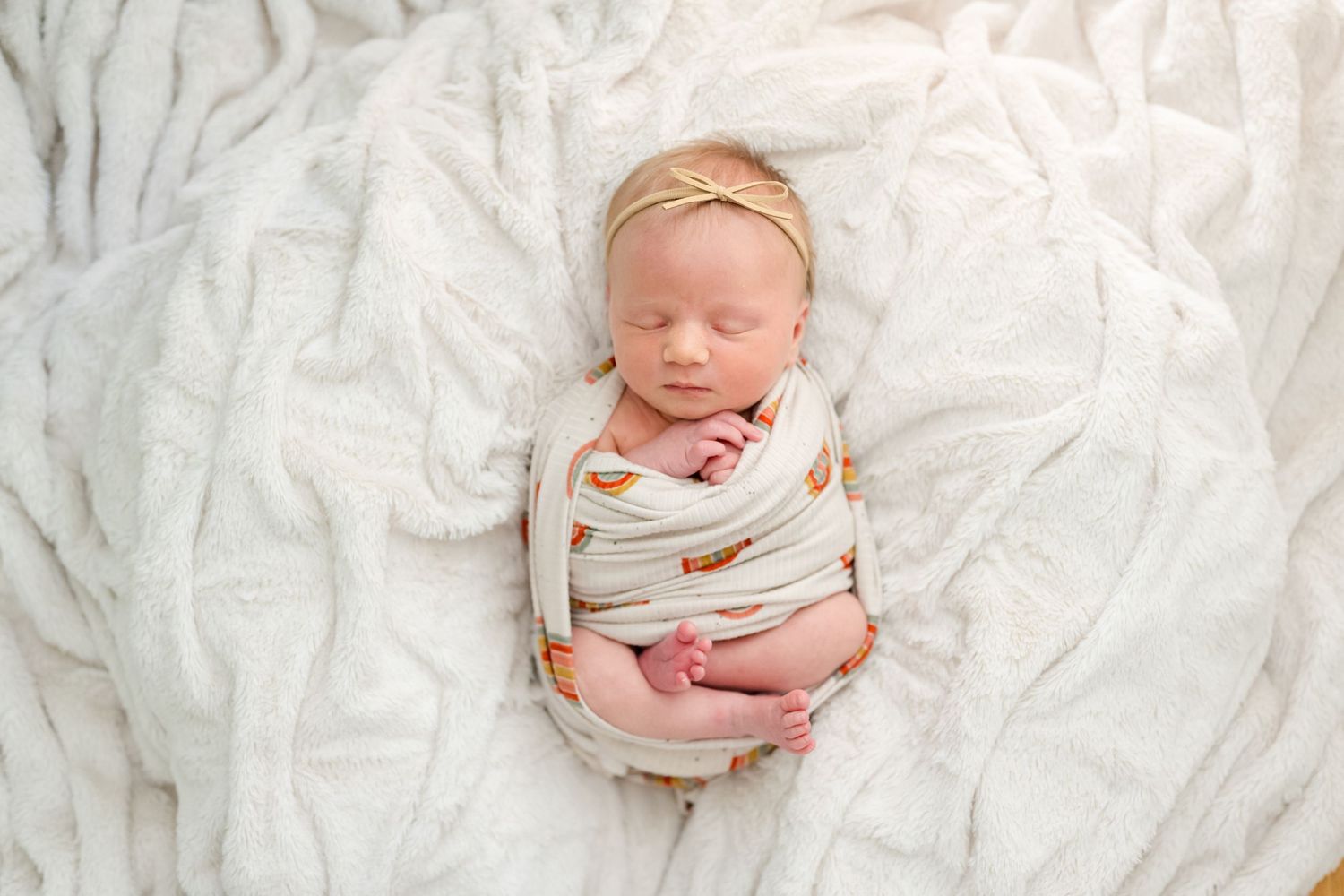 Sleeping newborn baby dressed in white lying on soft textured white fabric.