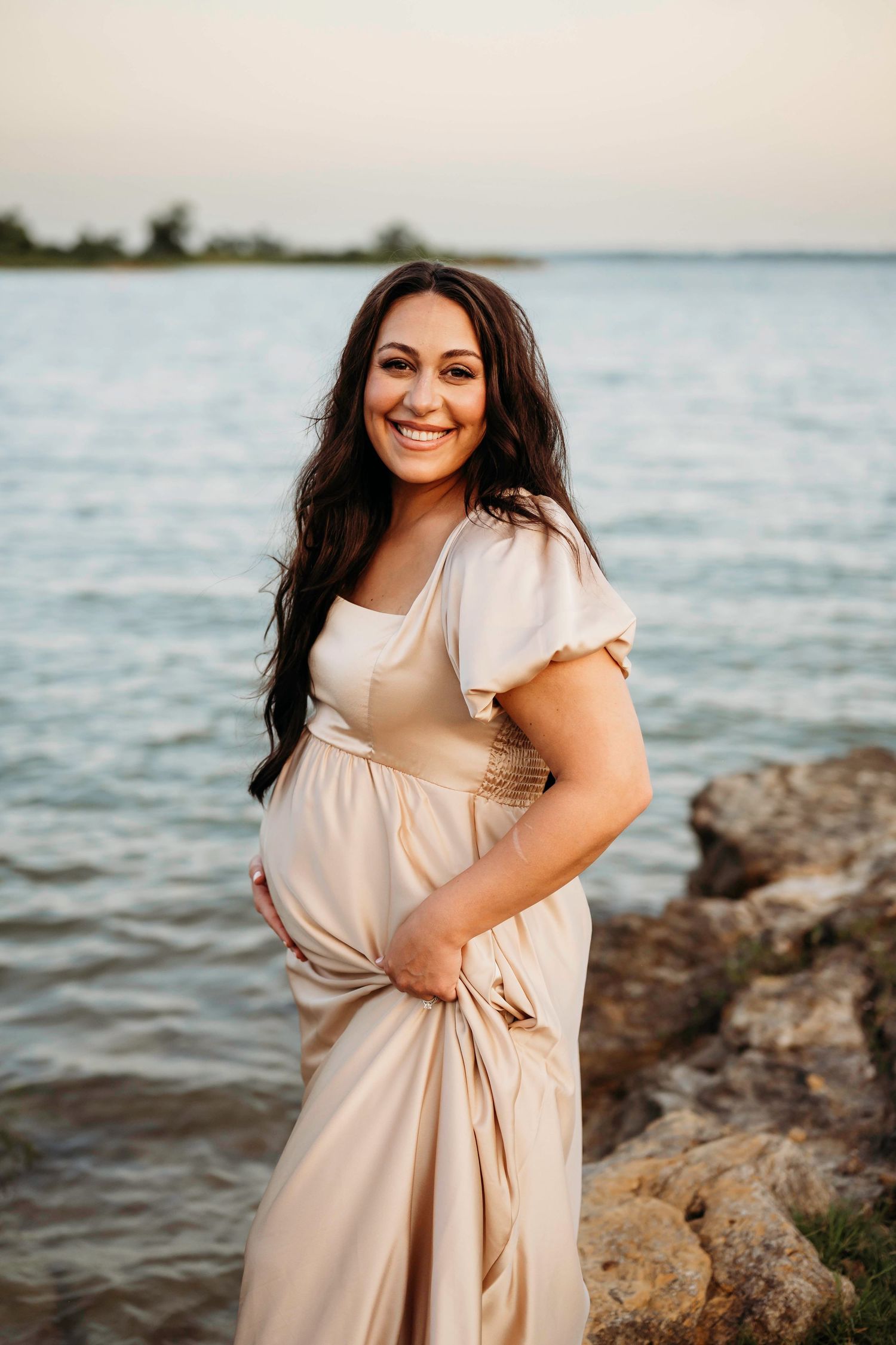 A woman in a beige dress poses by a rocky shoreline at sunset in a series of lifestyle photos.