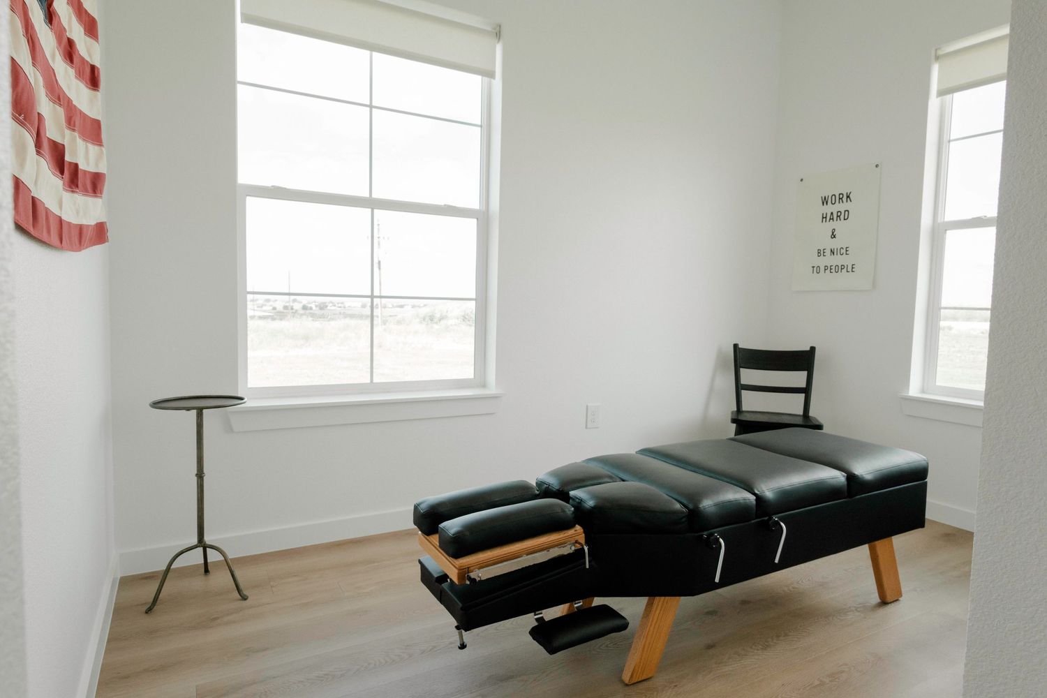 A modern chiropractic treatment room with an adjusting table and American flag decor on white walls.