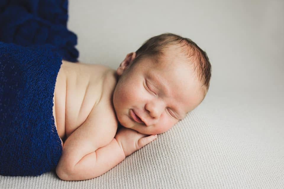 Peaceful newborn baby sleeping on soft white fabric.