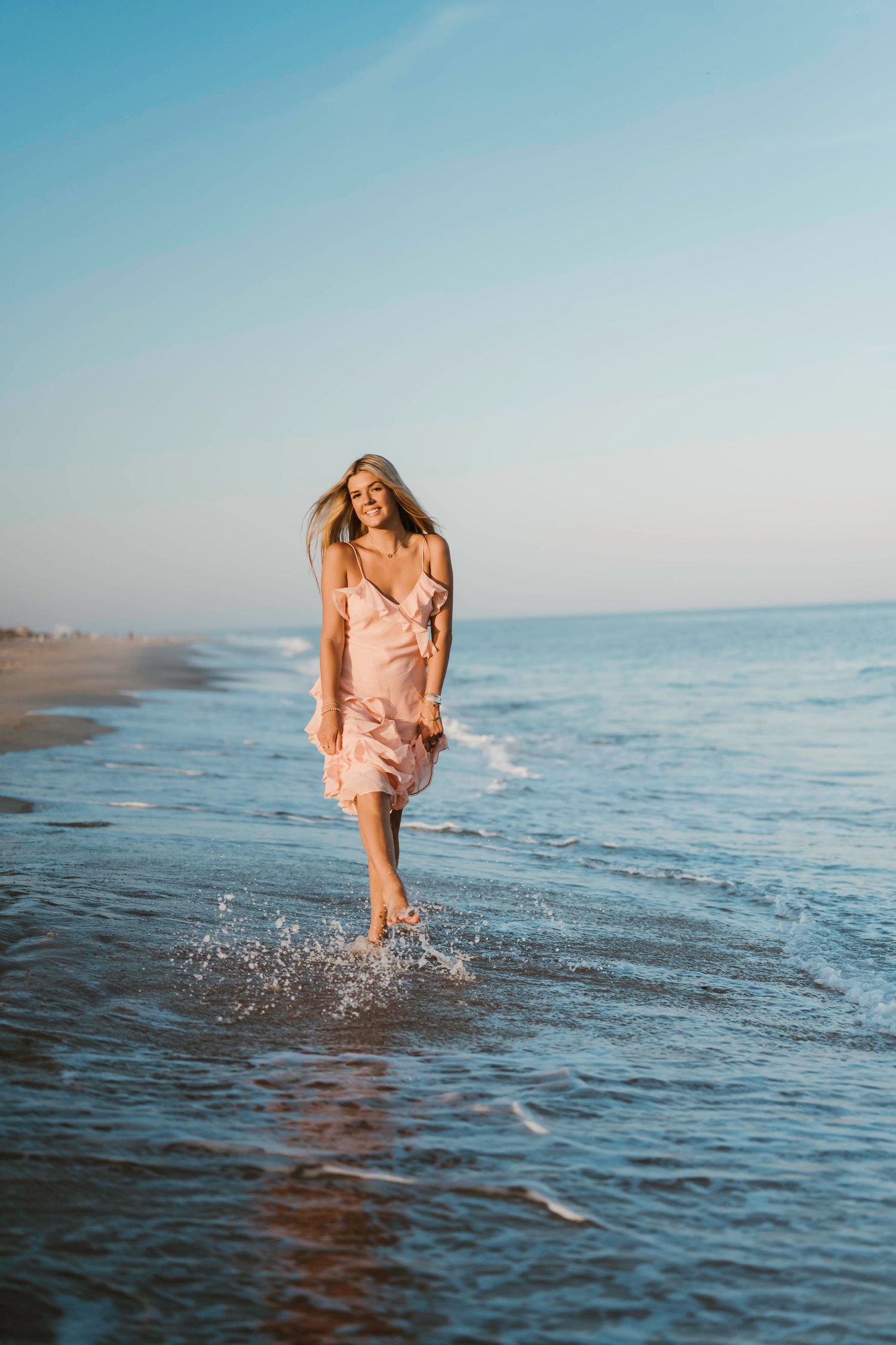A coral dress splashes through shallow ocean waters during a sunrise photoshoot.