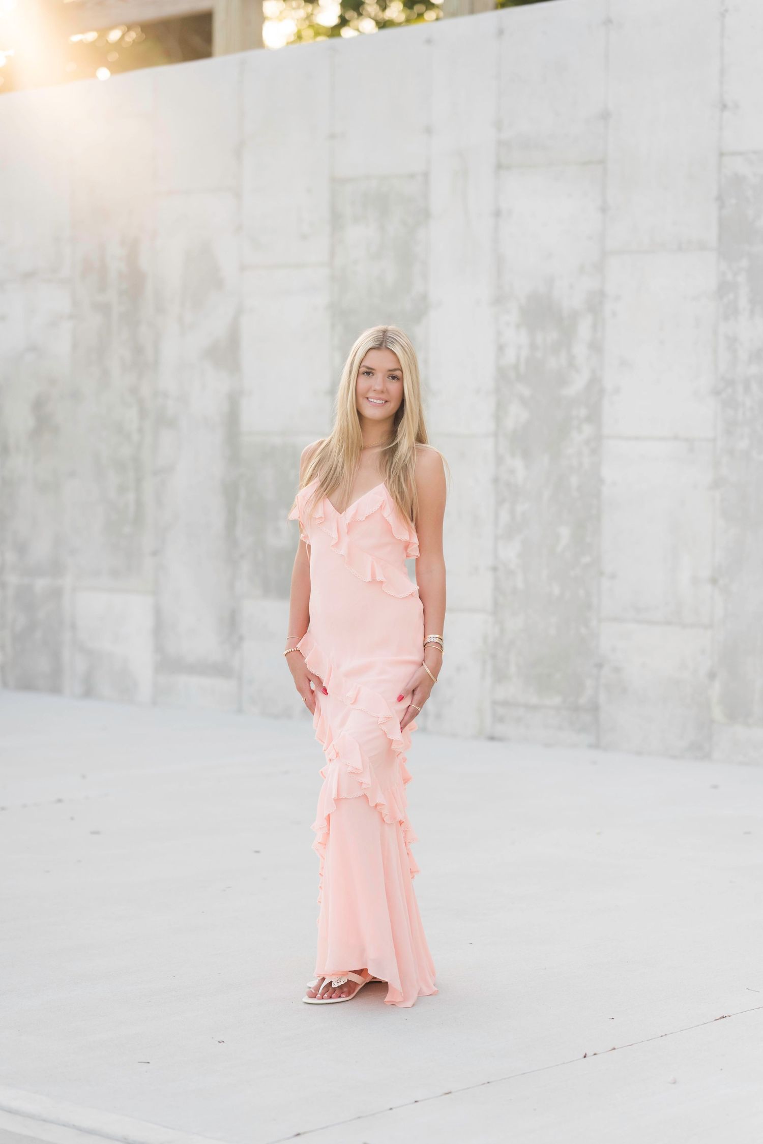 A series of four photos featuring someone in a light pink ruffled dress against a white concrete backdrop in natural lighting.