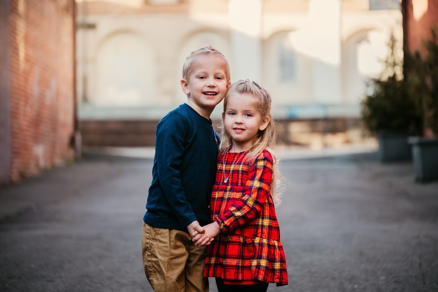Family photos against brick wall with children in red plaid and navy clothing.