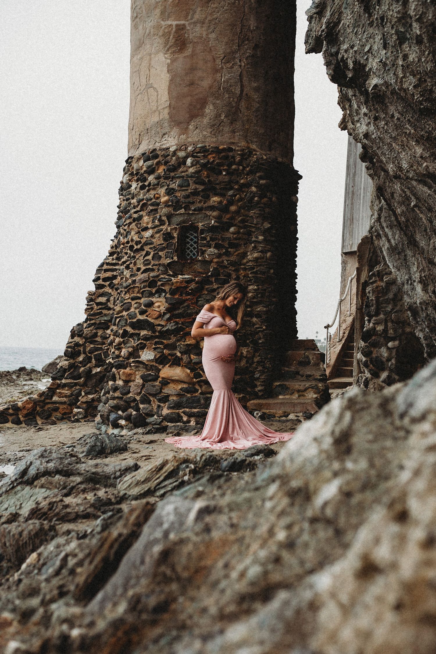 Figure in flowing pink gown poses dramatically against ancient stone fortress walls.
