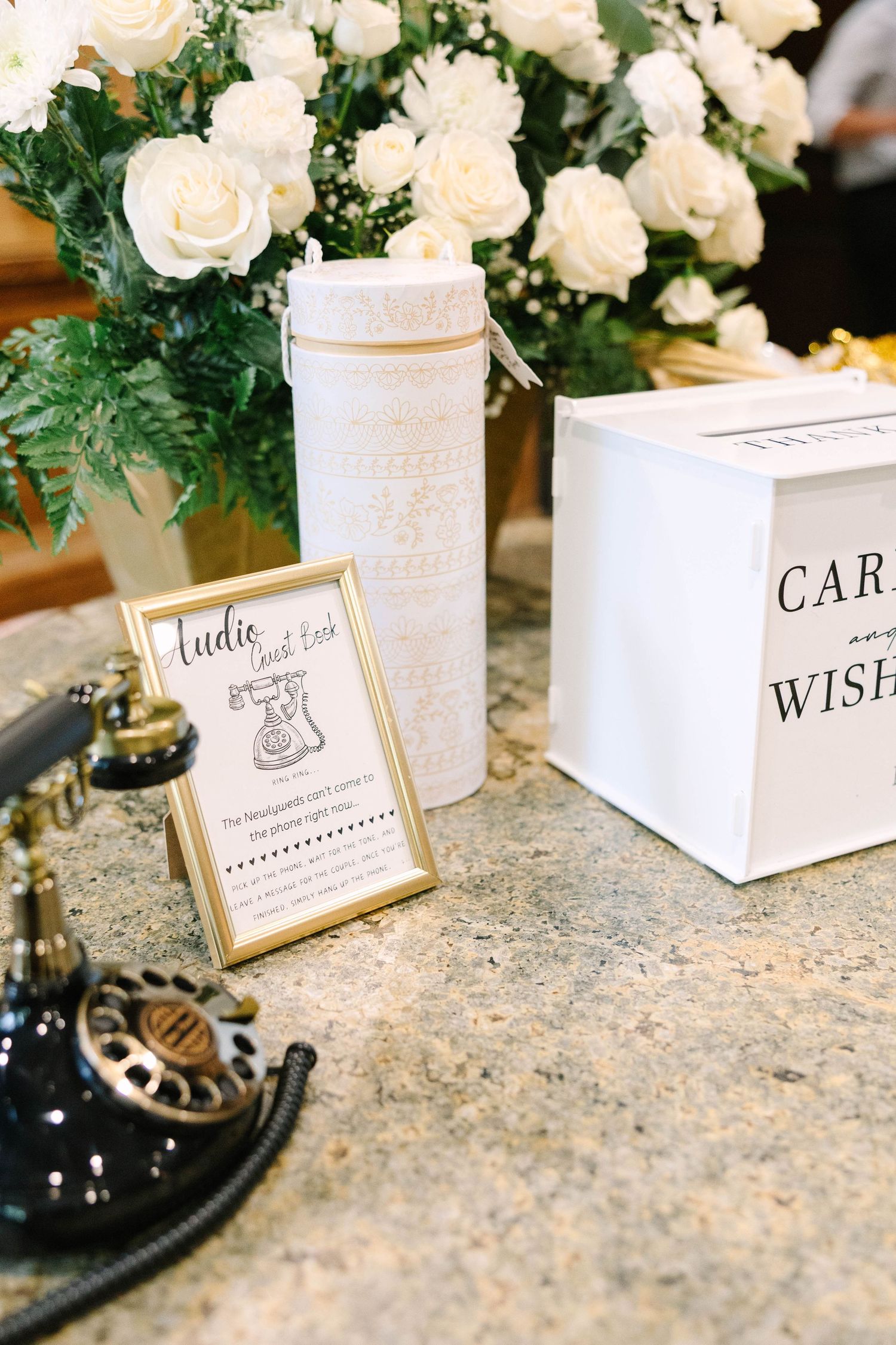 Vintage rotary phone audio guest book beside a white card box and cream roses at a wedding reception table.