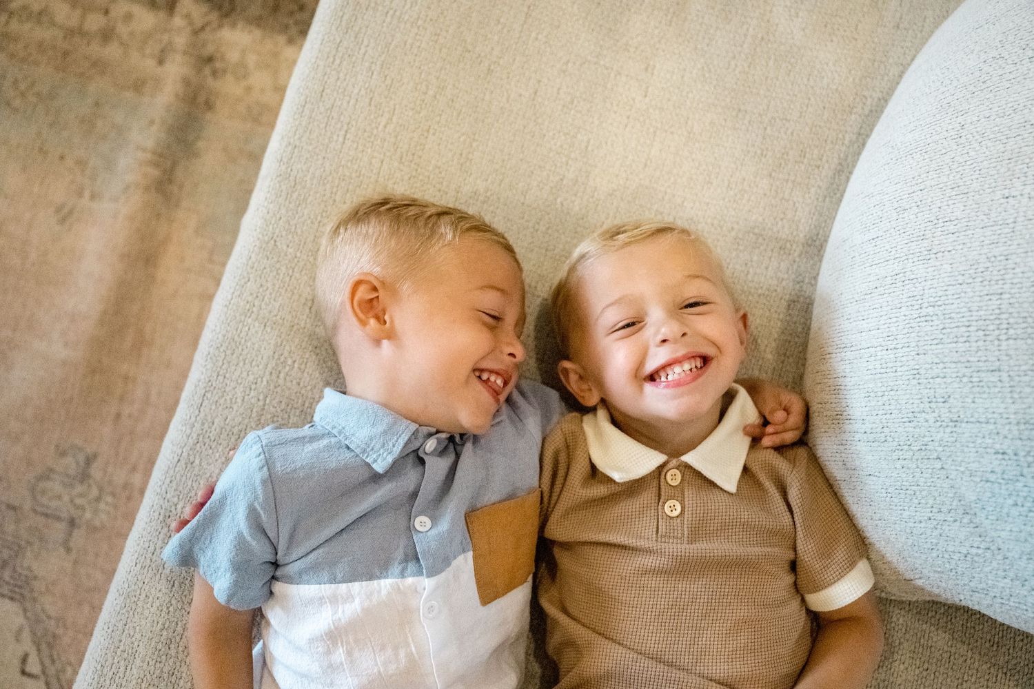 Two young children lying together on a light colored couch share sweet playful moments in matching outfits.