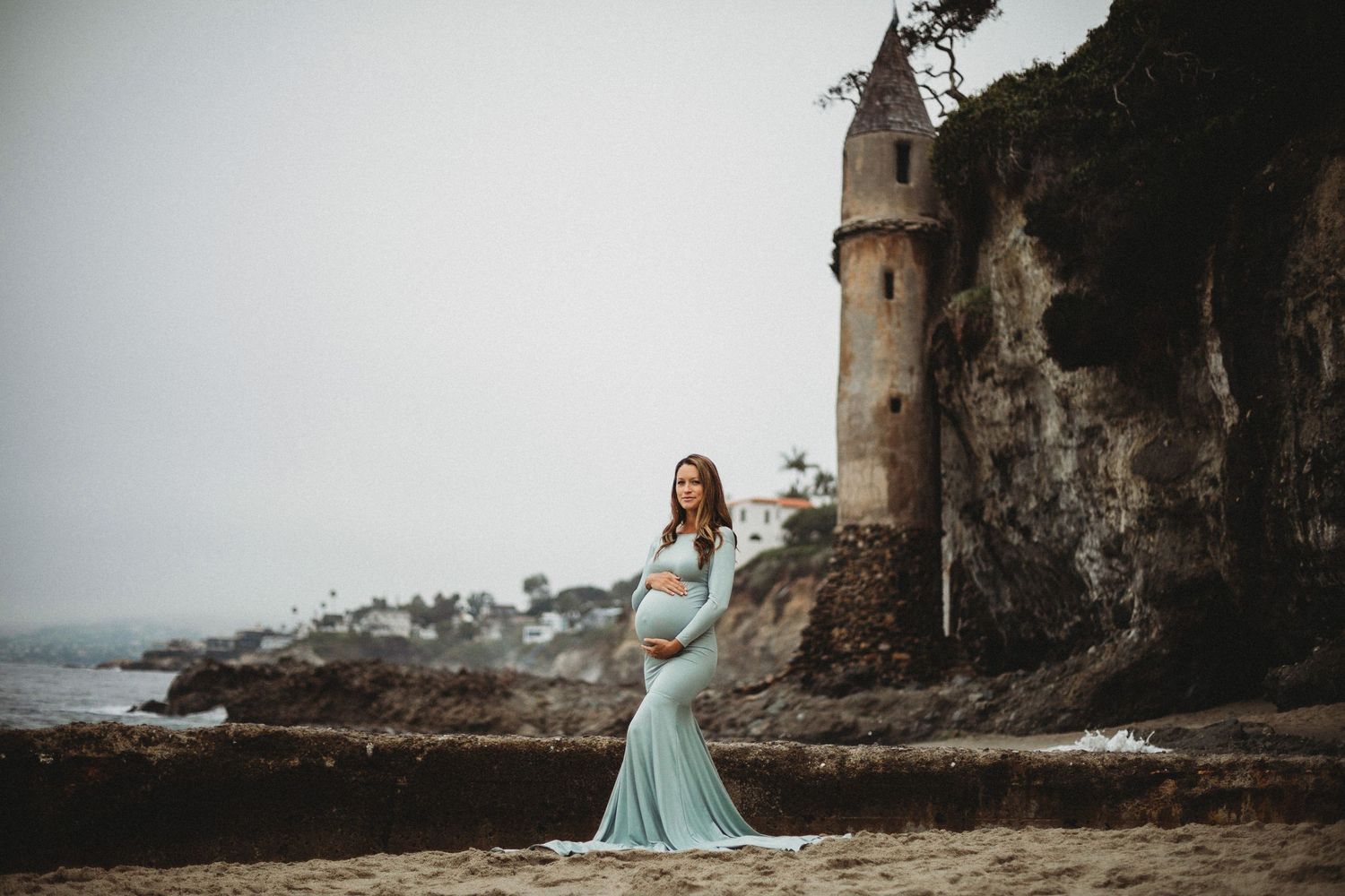 Elegant gown flowing in coastal breeze near historic stone watchtower with ocean views.