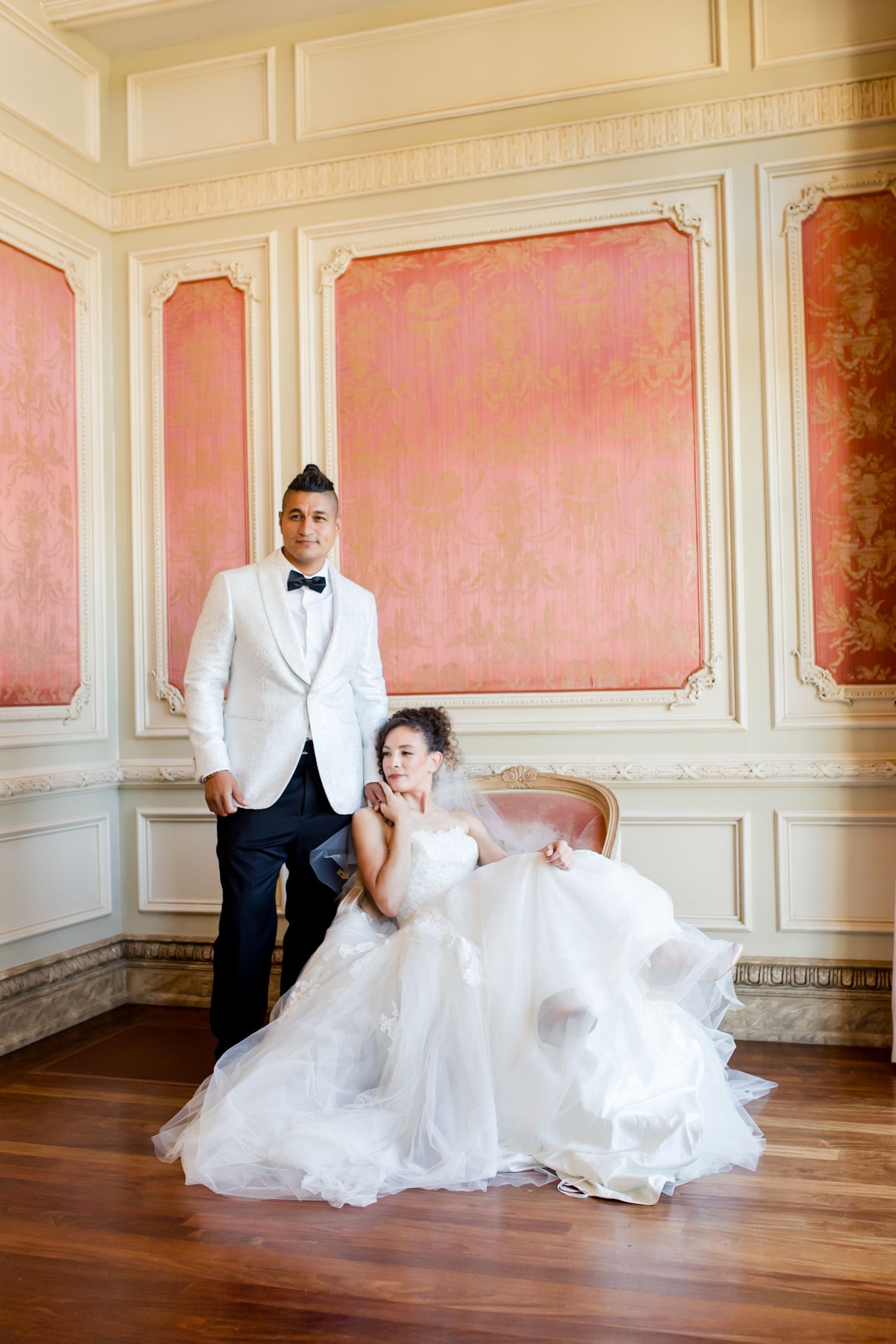 Elegant wedding portraits in a pink-walled room with ornate white molding and hardwood floors.