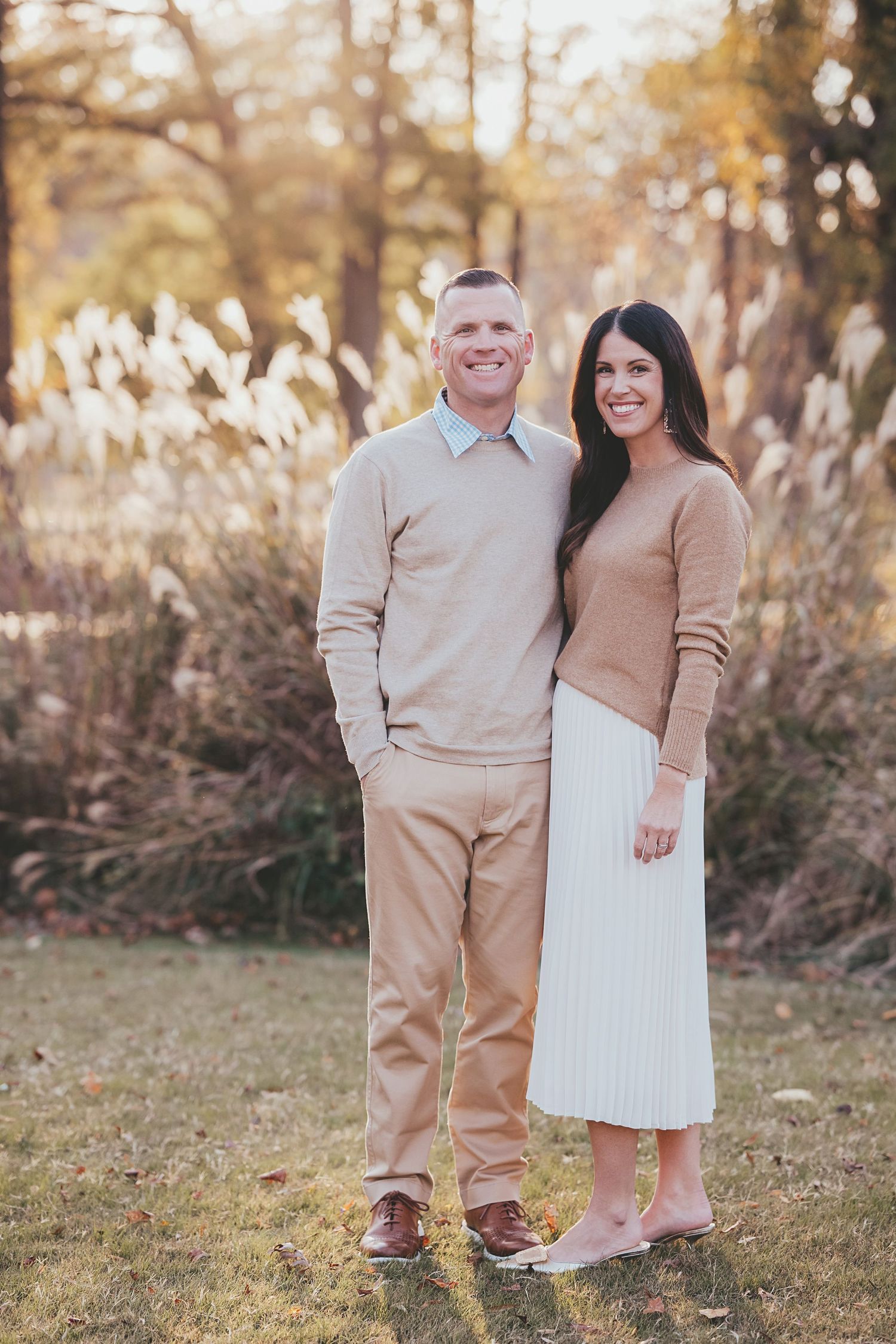Couple in coordinated beige outfits standing together outdoors during golden hour.