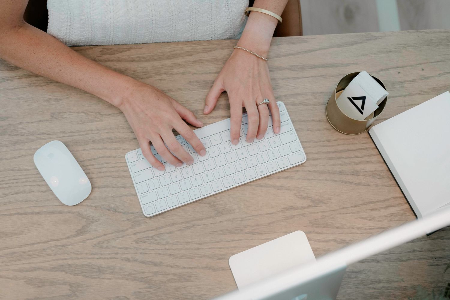 Person working at wooden desk with white wireless keyboard and mouse setup in minimalist workspace setting.