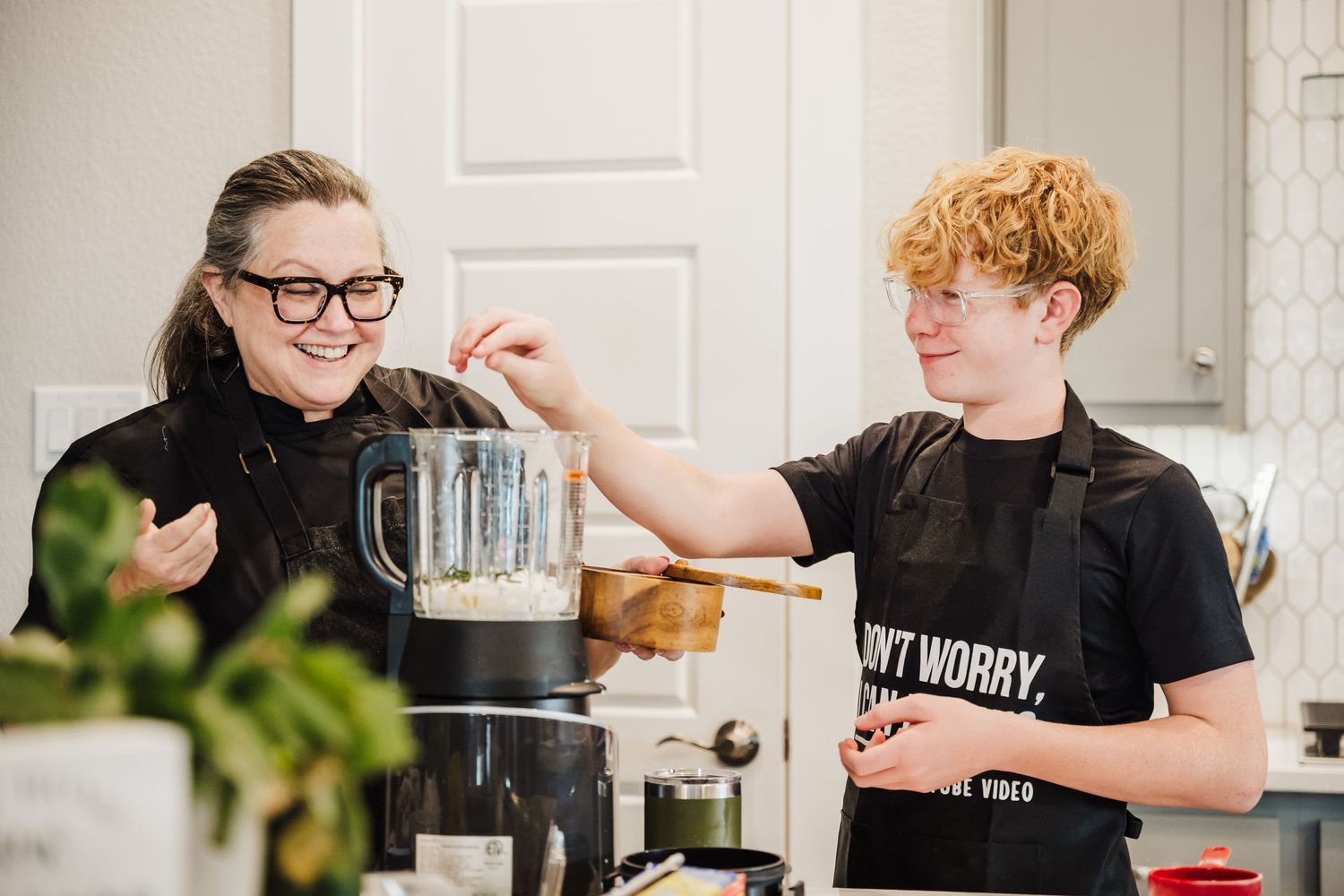 Two people in a kitchen working together with a blender while preparing food and beverages.