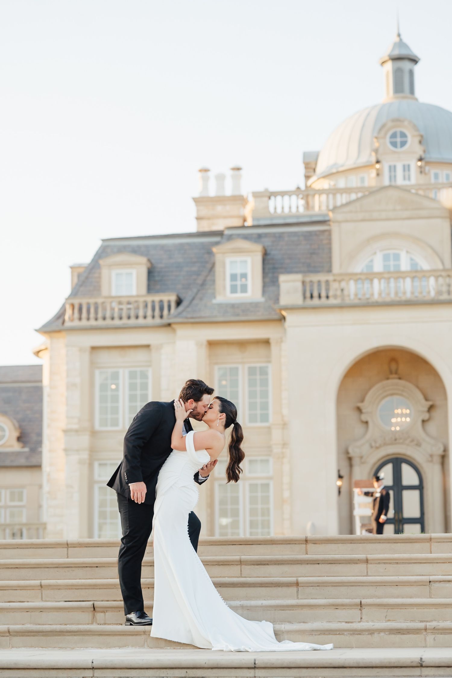 Elegant wedding couple poses on grand steps of ornate domed building.