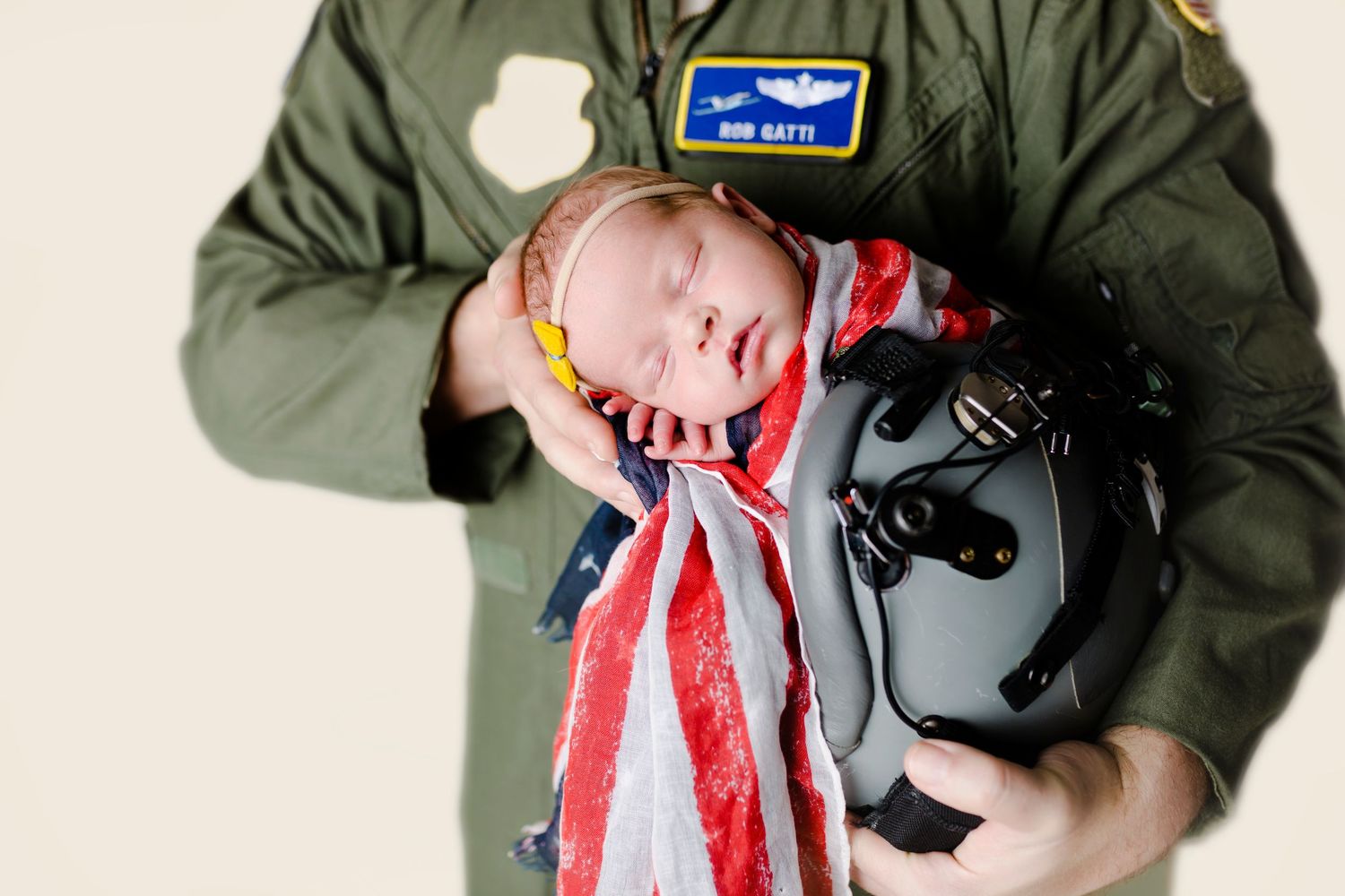 A sleeping baby wearing a red and white striped scarf rests against a flight suit and helmet.