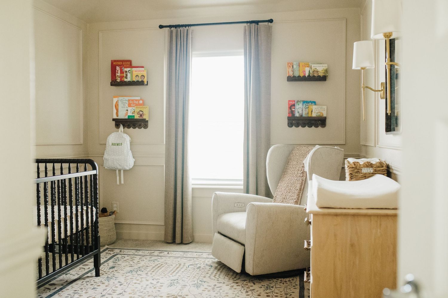 A bright and airy nursery room features a white crib, glider chair, and floating shelves with baby essentials.