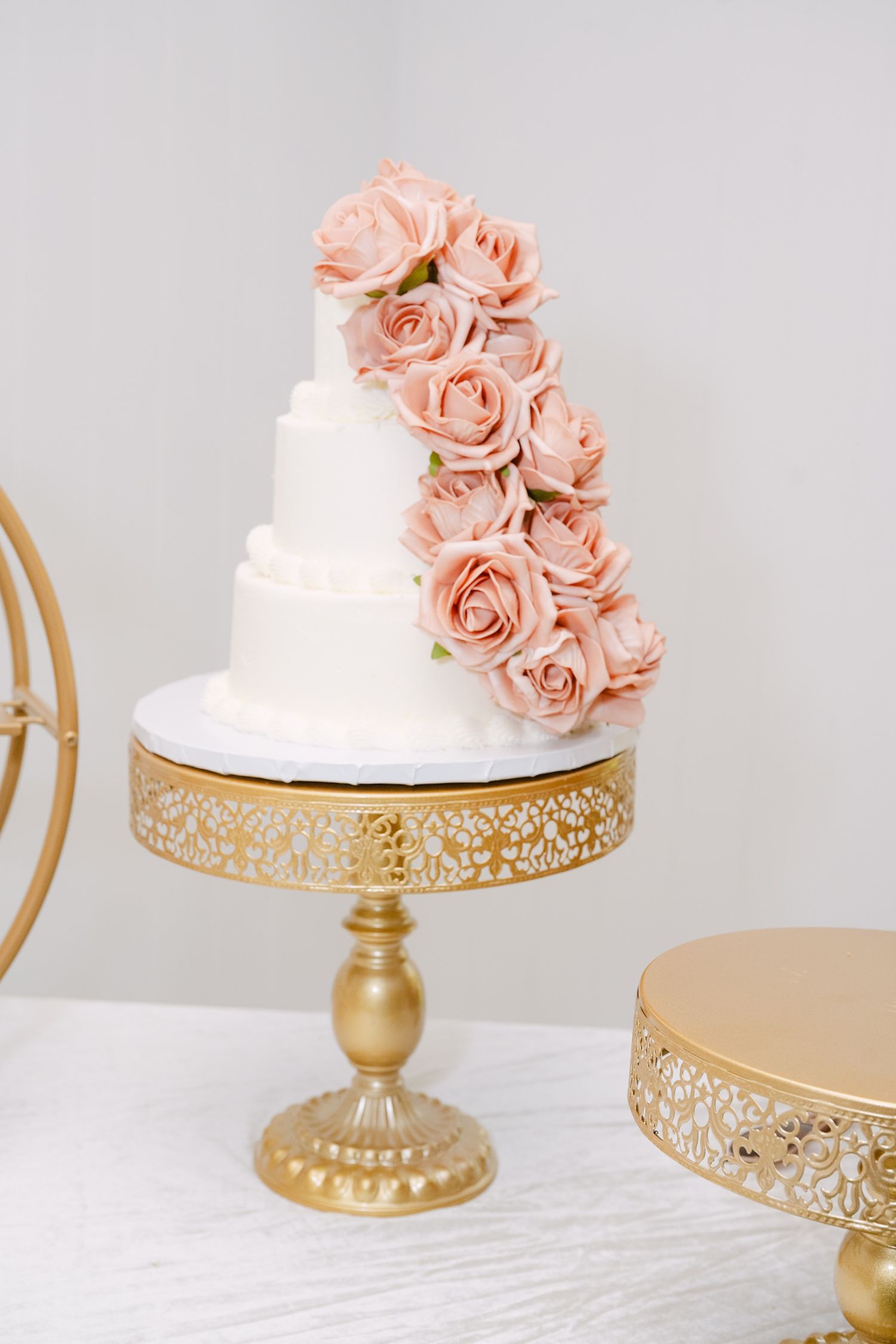 Elegant white wedding cake decorated with peach roses on a gold vintage-style pedestal cake stand with intricate detailing.