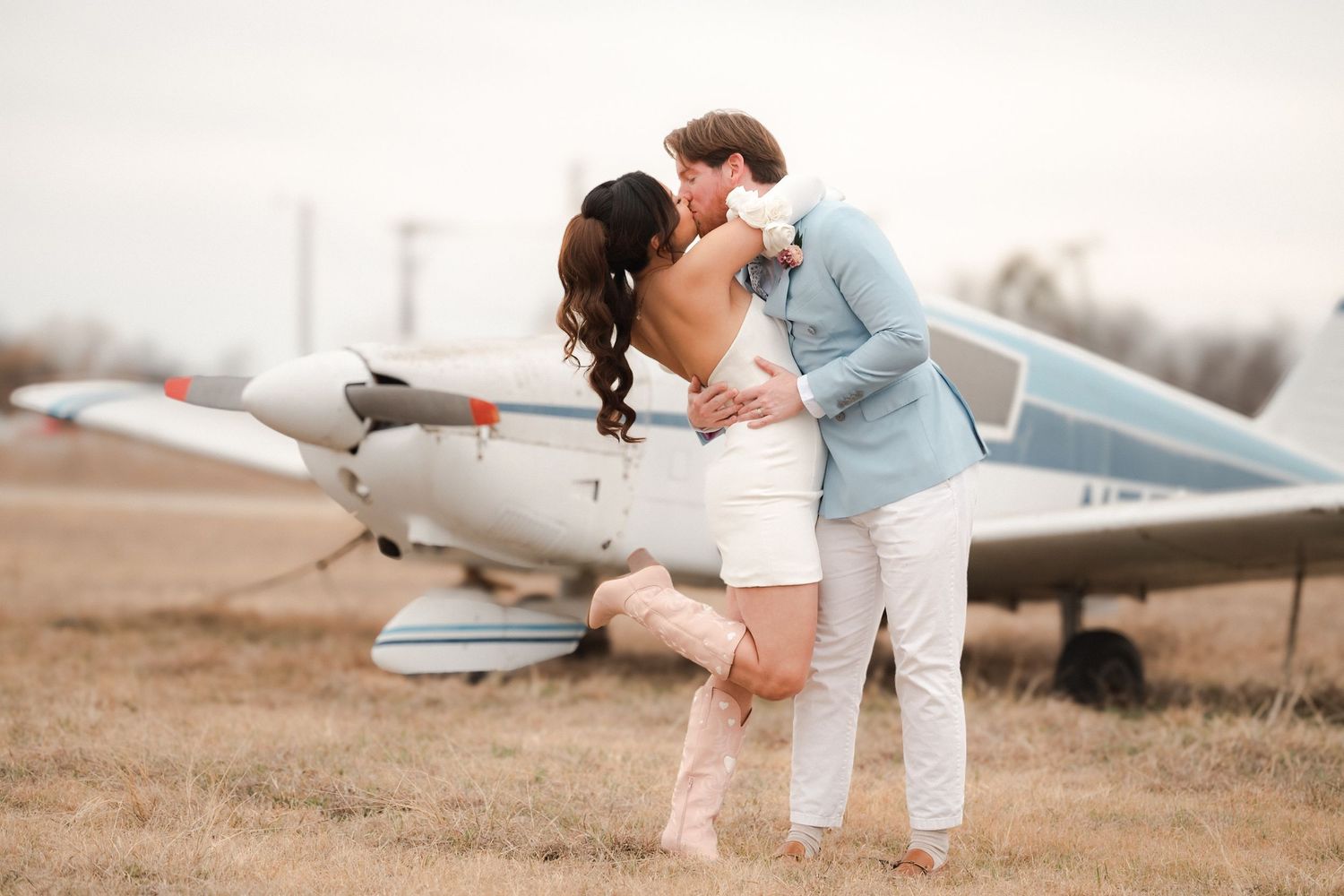 Couple in casual attire shares tender moments by a small airplane on an airstrip during their engagement shoot.