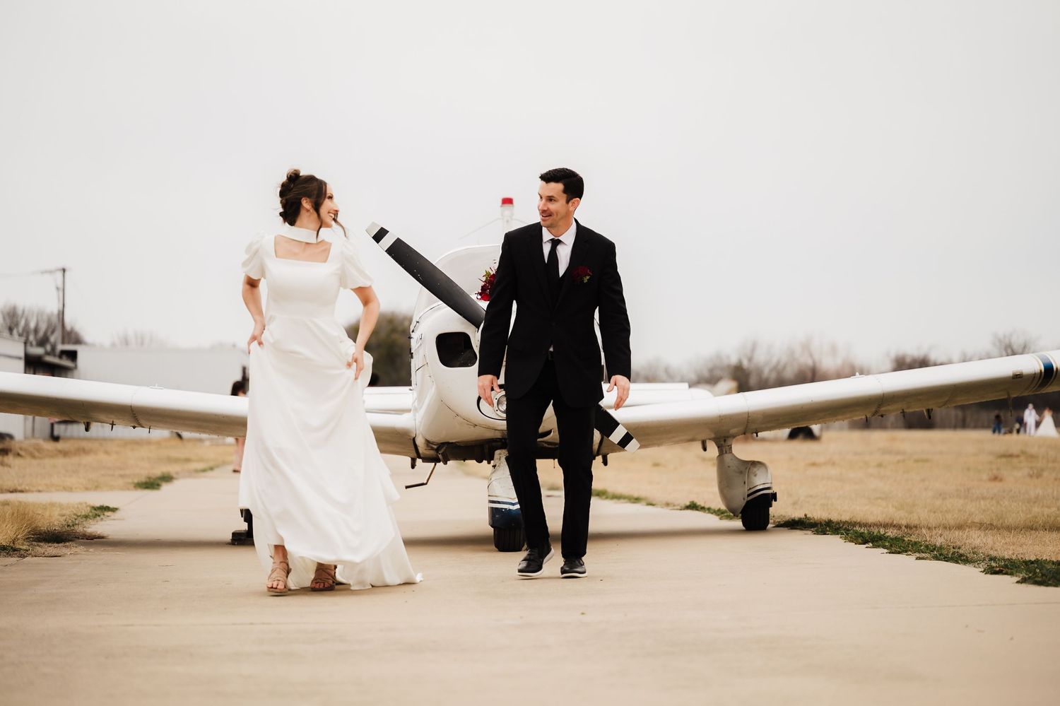 Bride and groom share romantic moments near vintage aircraft during sunset wedding photoshoot at airfield.