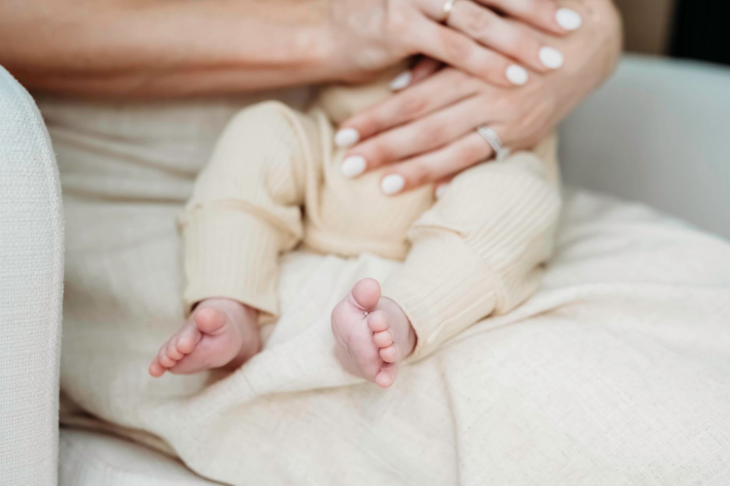 Close-up of tiny baby feet and hands on cream colored bedding.