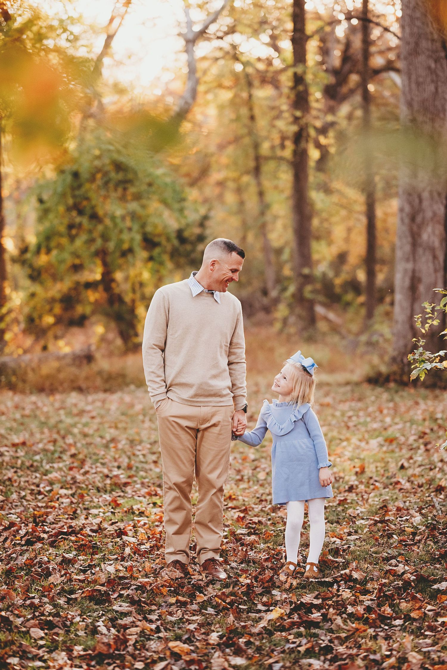People interact playfully among fallen autumn leaves in a wooded setting.