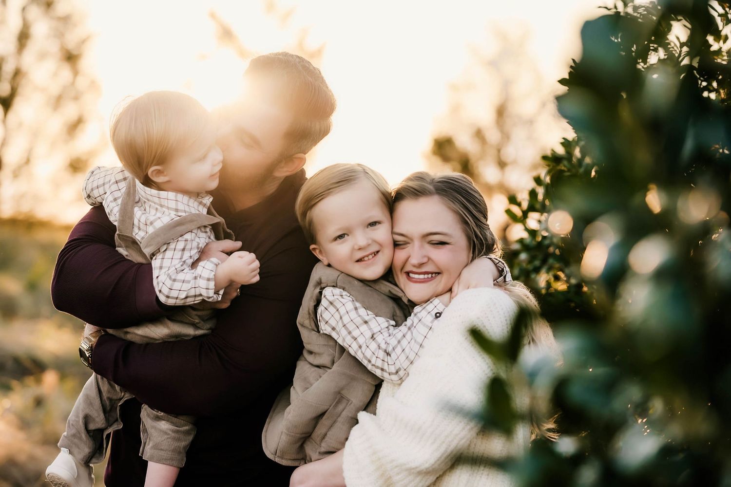 A loving family embraces in a golden sunset while surrounded by lush greenery and bokeh lights.