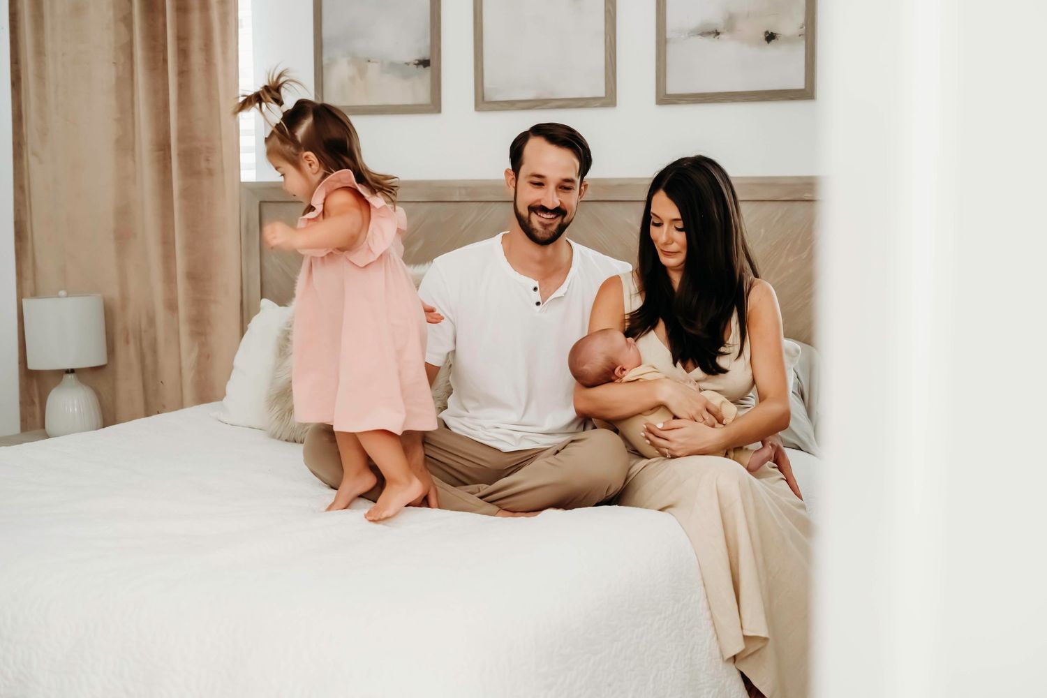 Family relaxing together on bed with newborn in neutral colored room.