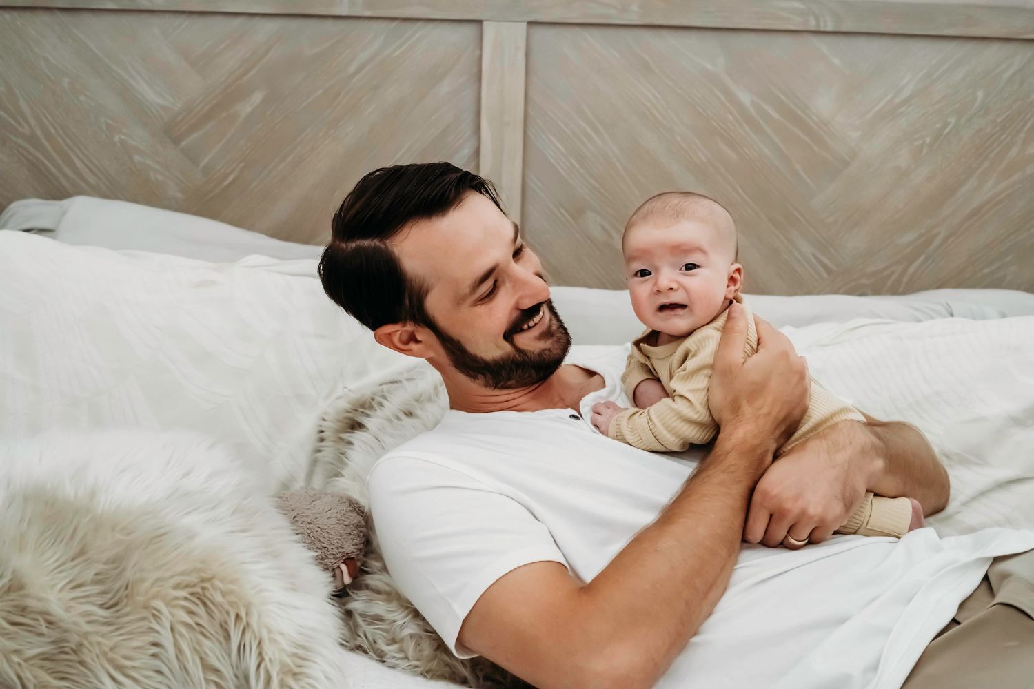 Tender moment with baby on white bedding in natural light.