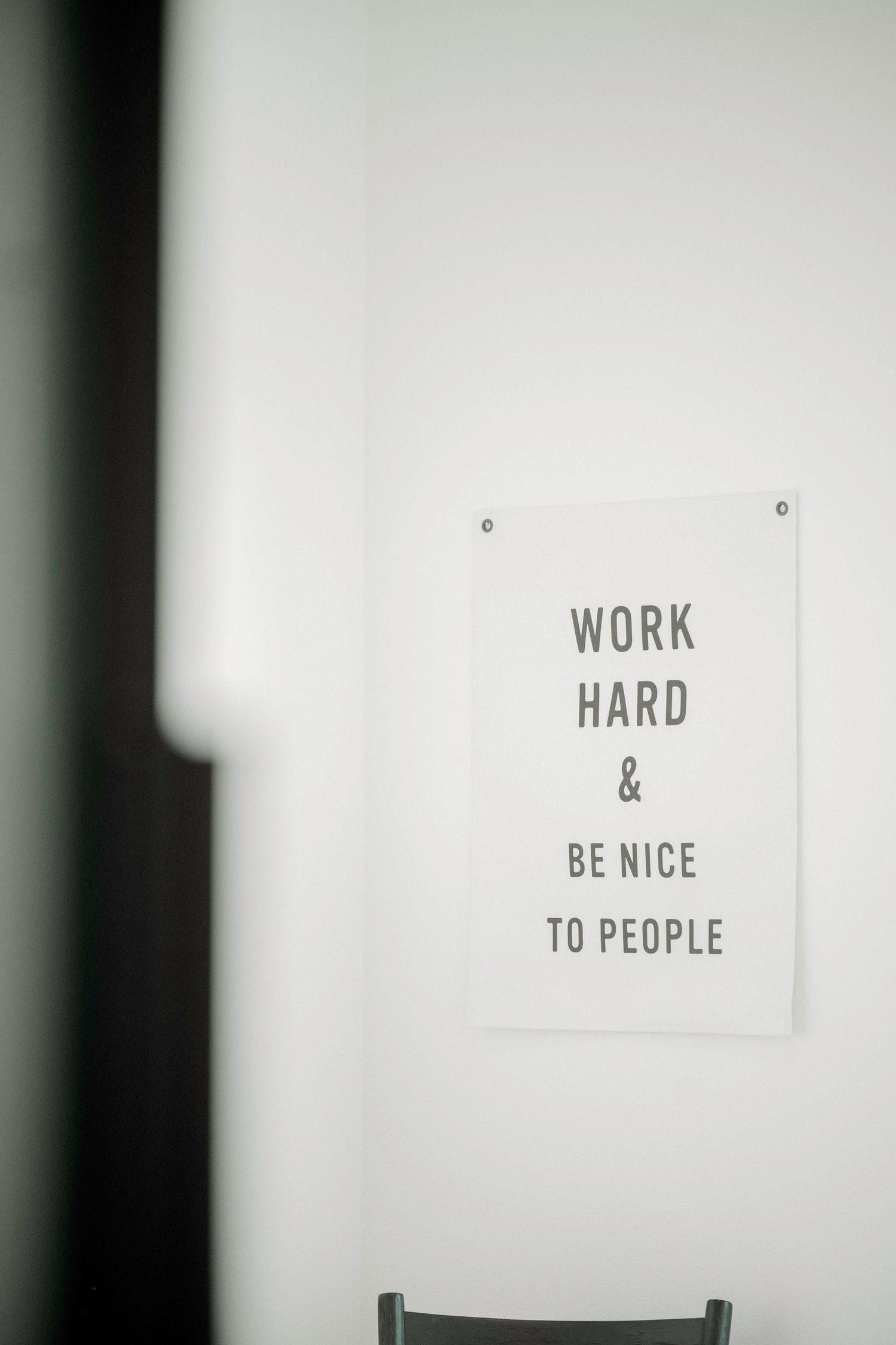 Three motivational signs on white wall reading 'Work Hard & Be Nice To People'.