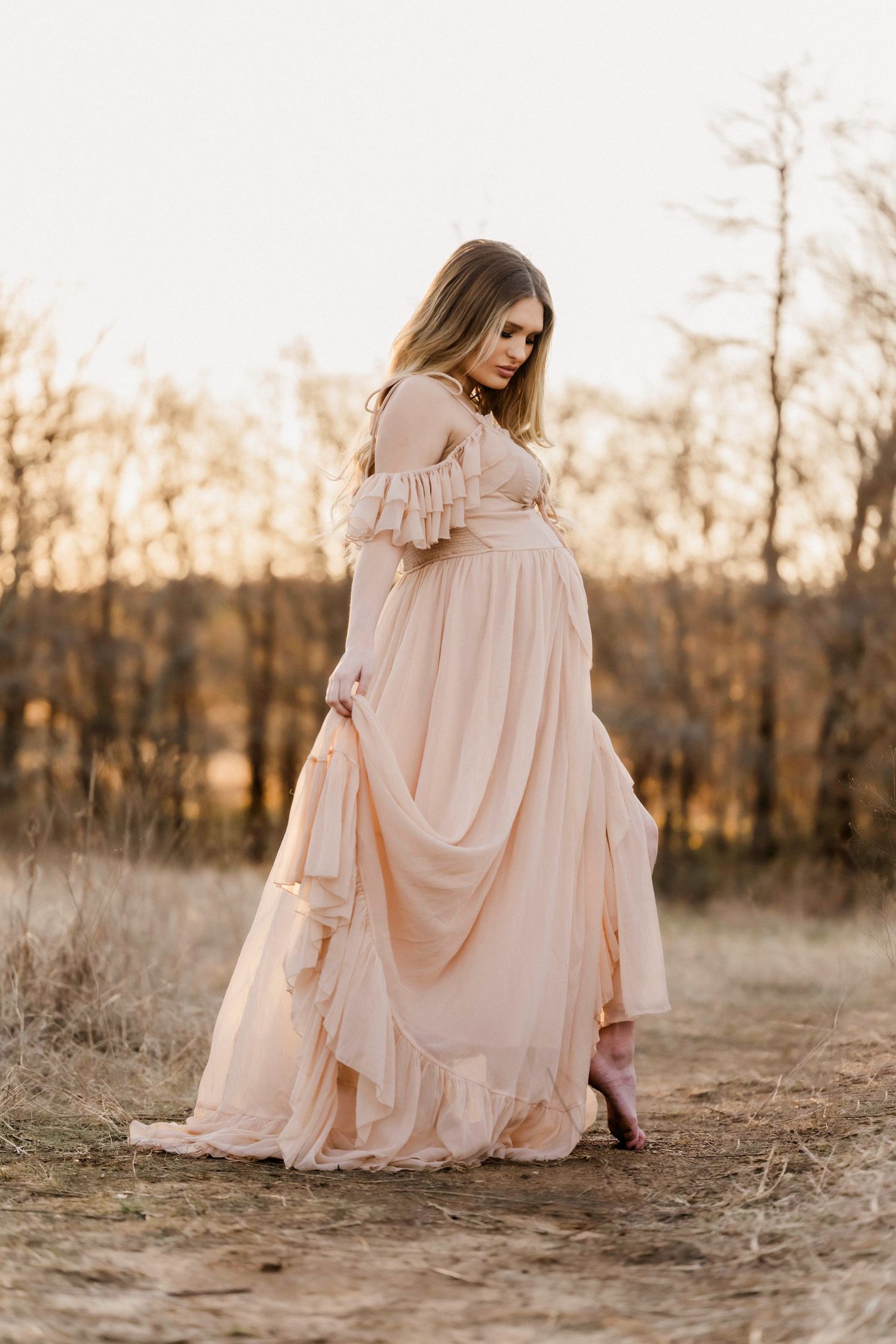 Elegant maternity portrait featuring a billowing blush gown in a natural outdoor setting.