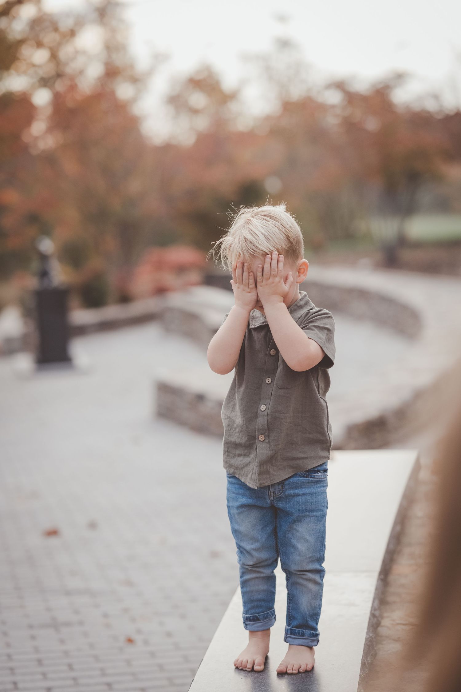 Small child playing peek-a-boo on cobblestone path during autumn.