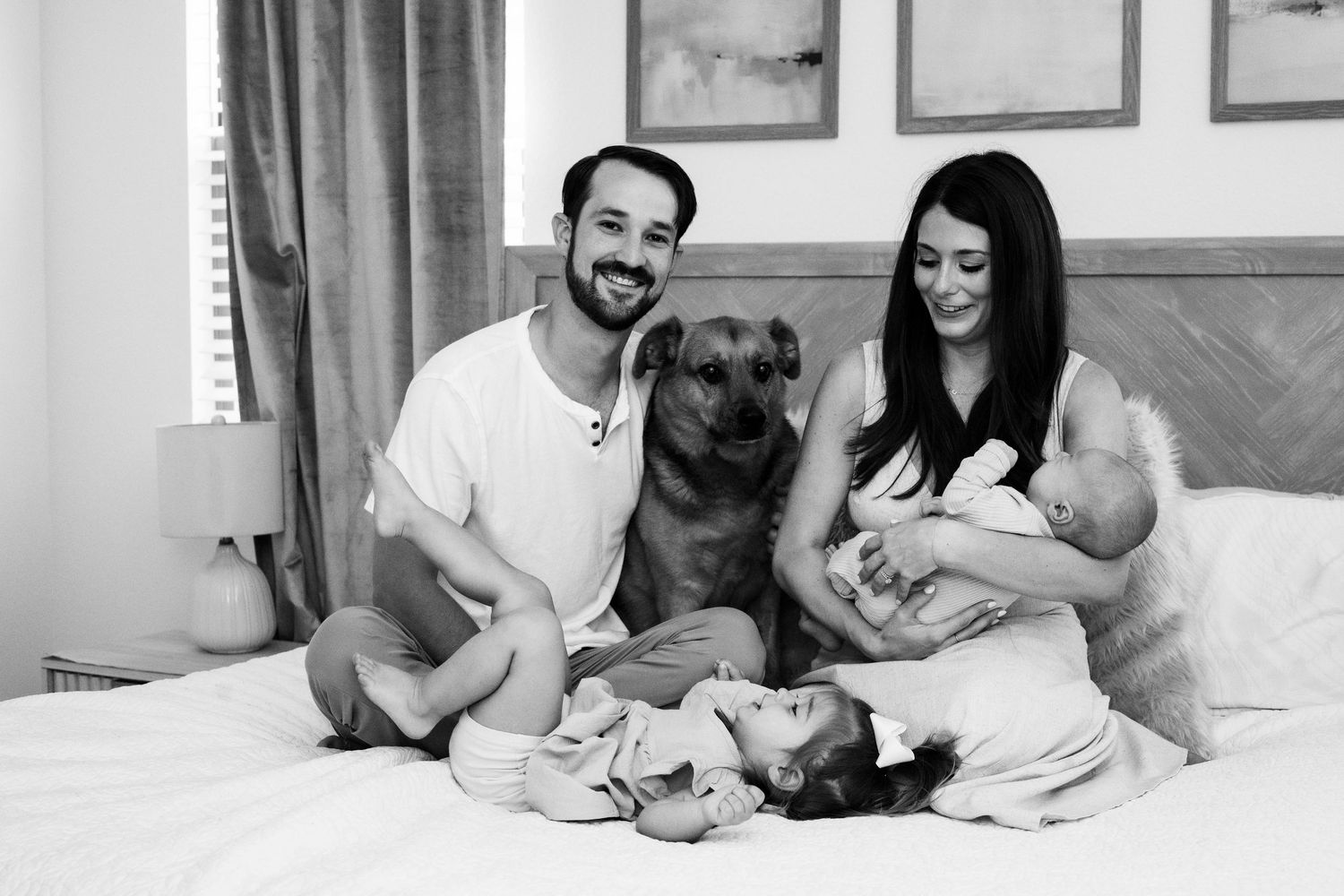 Intimate lifestyle photography session of a couple cuddling with their newborn baby on a white bed.