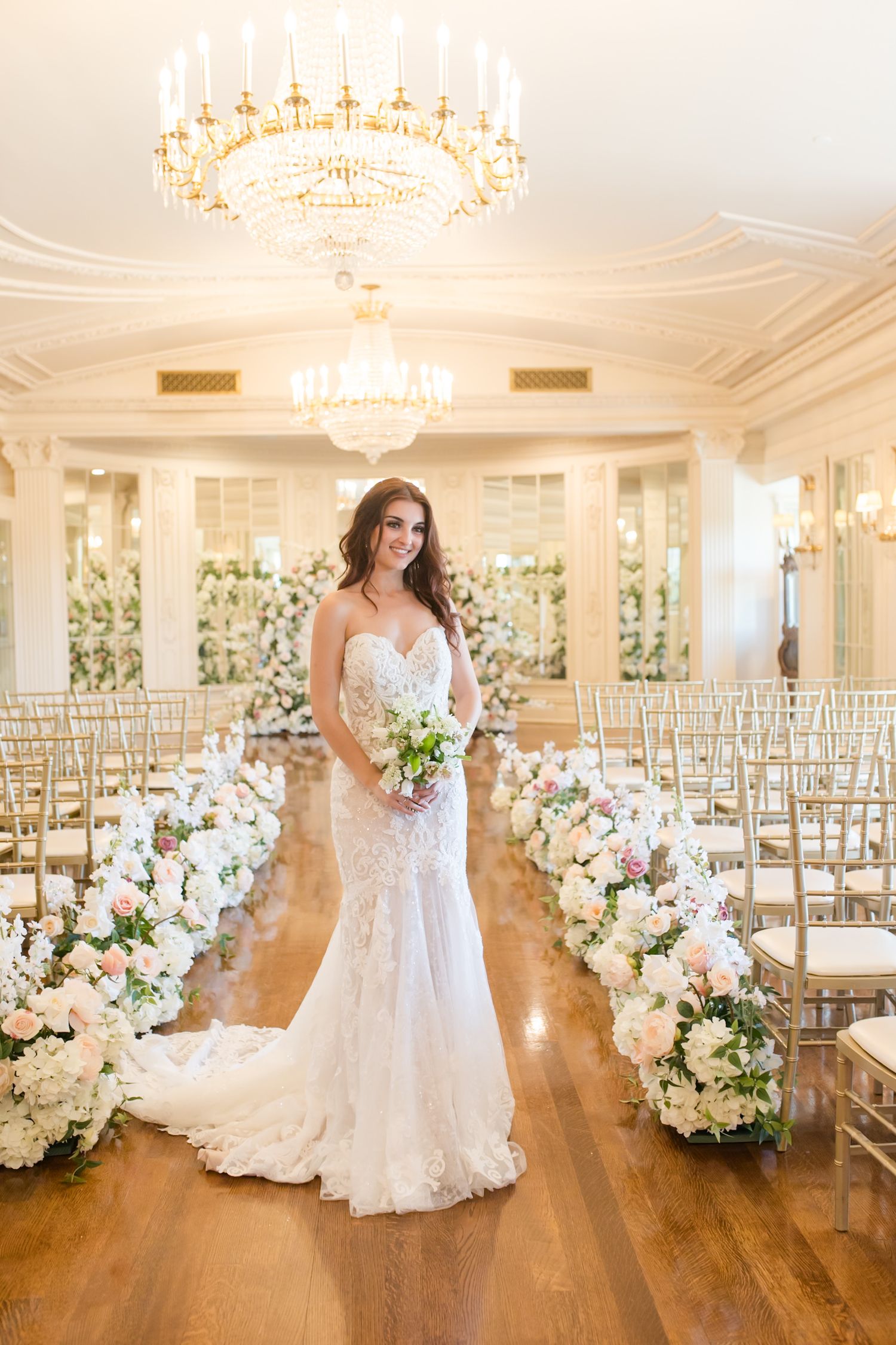 Elegant wedding venue with hardwood floors, crystal chandeliers, and floral aisle decorations.