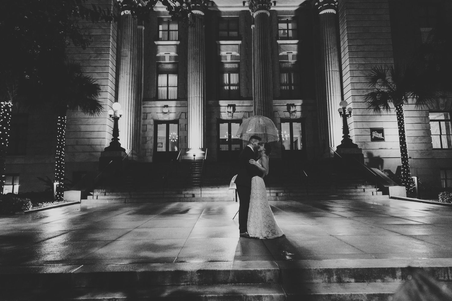 Black and white panoramic photo of an illuminated grand building entrance at night with dramatic shadows.