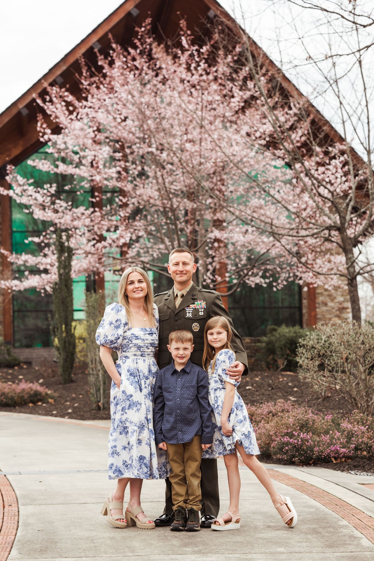 Family photoshoot near a rustic building with blooming cherry blossoms in spring.