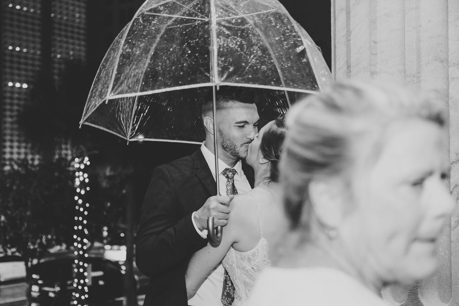 A black and white photo series shows people holding umbrellas while dancing at what appears to be a wedding celebration.
