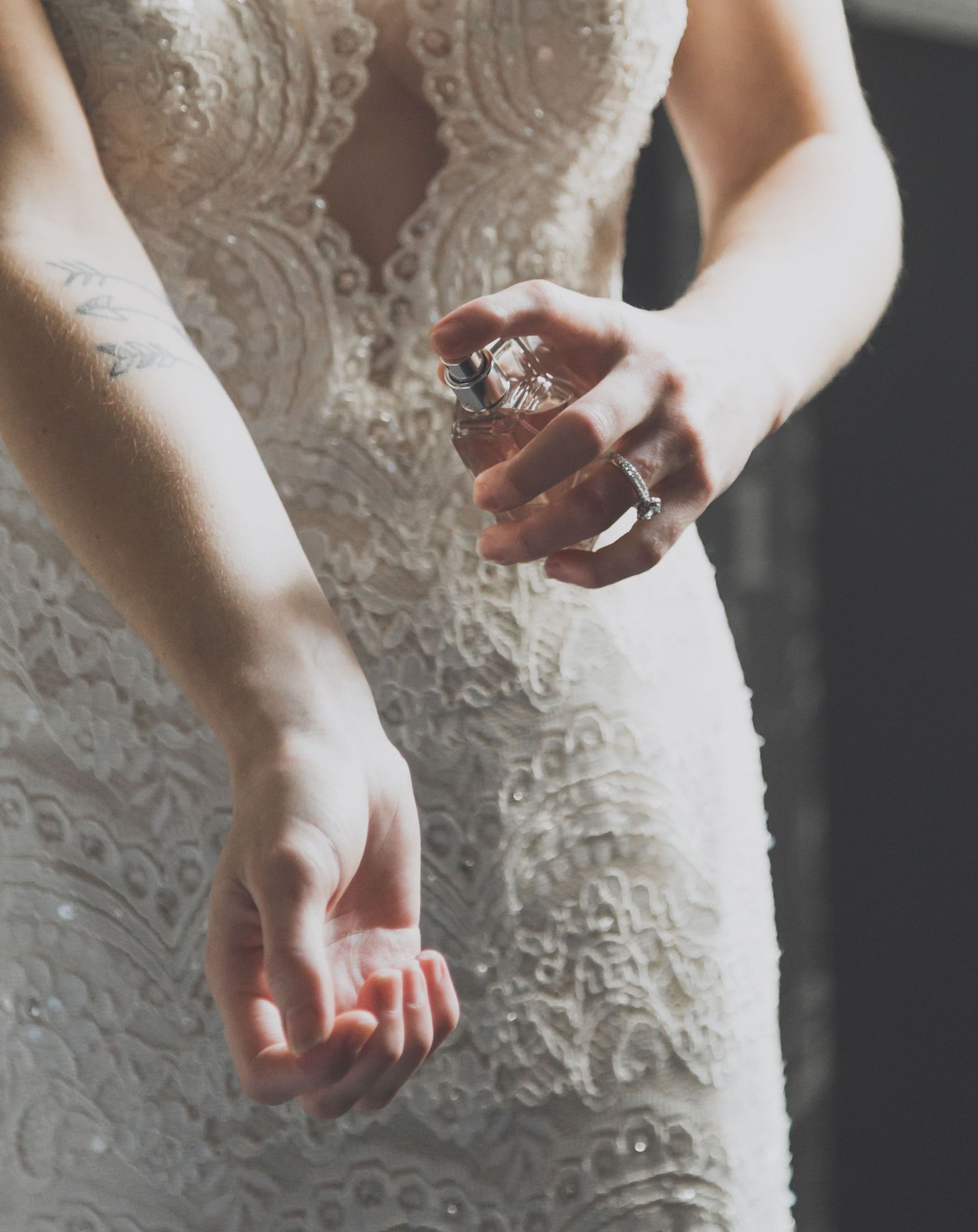 Close-up details of intricate lace patterns and beadwork on a white wedding dress with hands in view.
