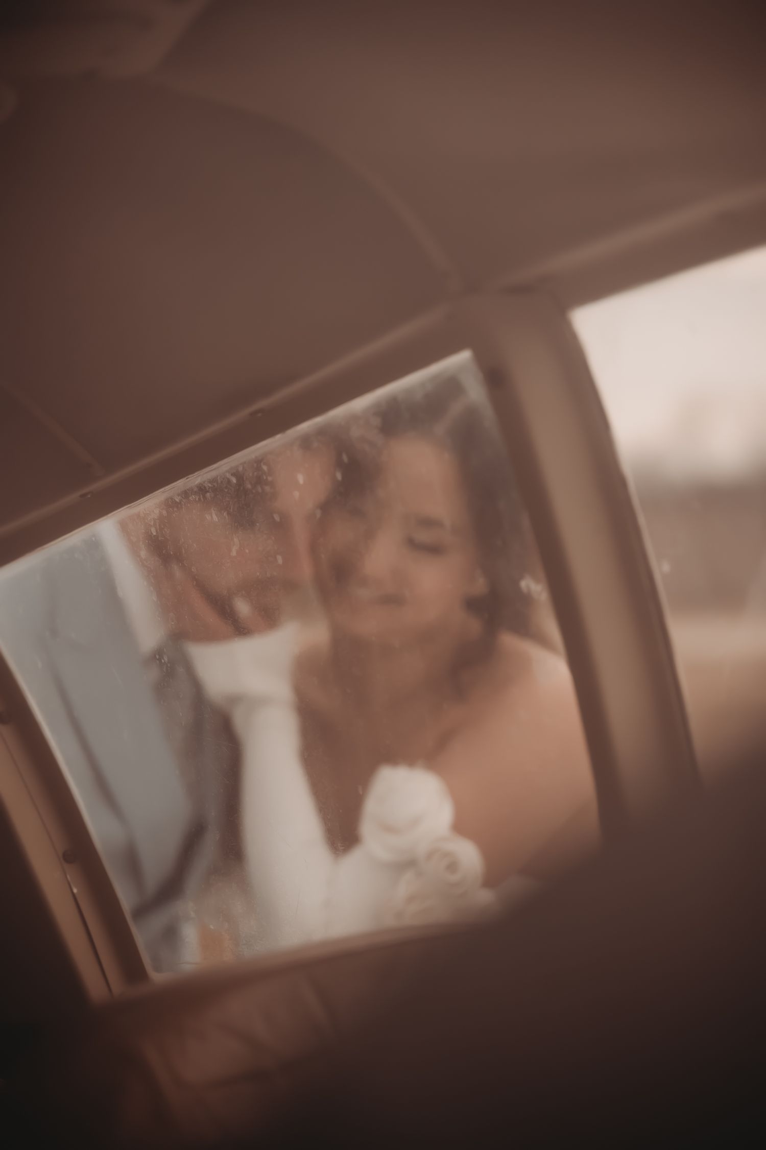 Intimate wedding moments photographed through a car window with a soft brown vintage filter effect.