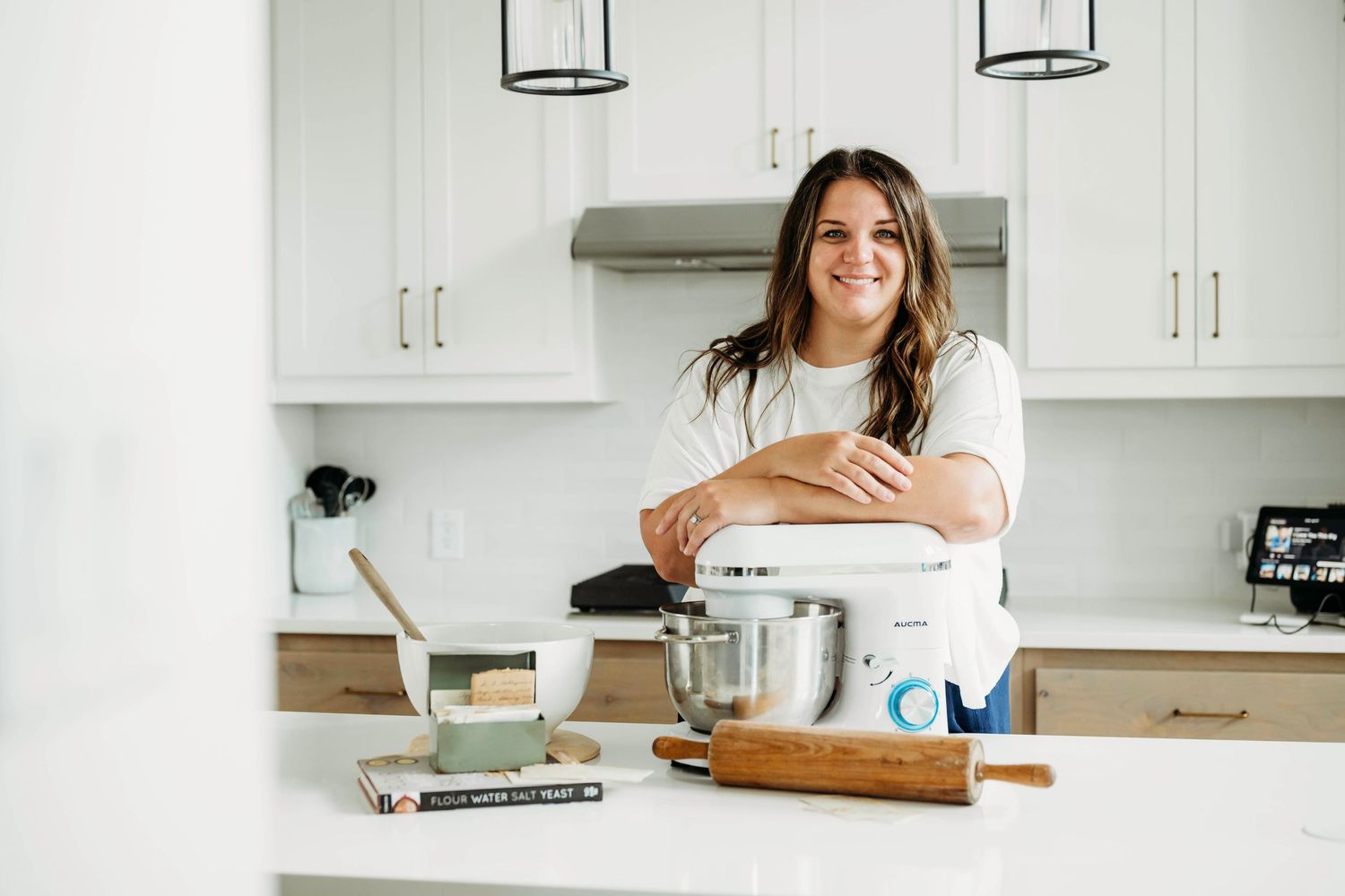 Person working at white desk in bright modern kitchen with laptop and coffee mug.