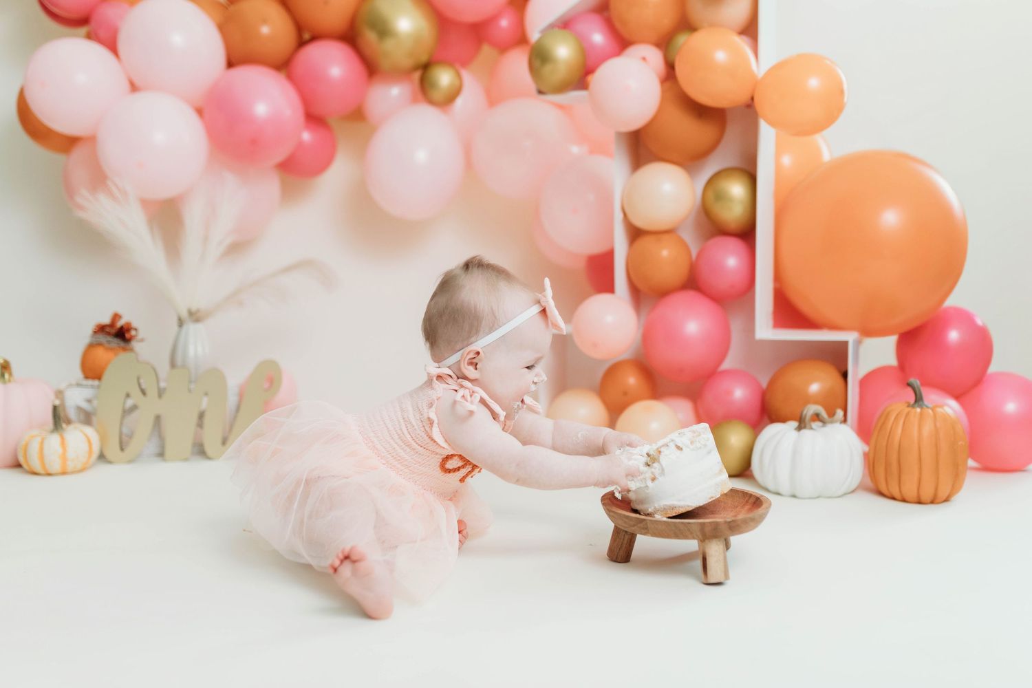 Pink and peach balloon garland with pumpkins creates an elegant autumn party display with soft pastel decorations.