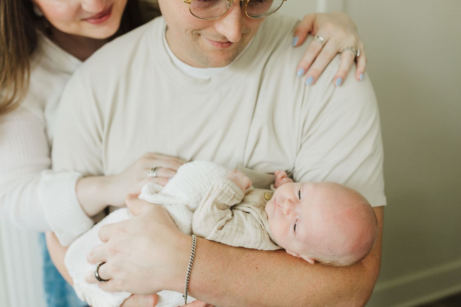 A person in a white t-shirt holds and comforts a sleeping newborn baby in a peaceful indoor setting.
