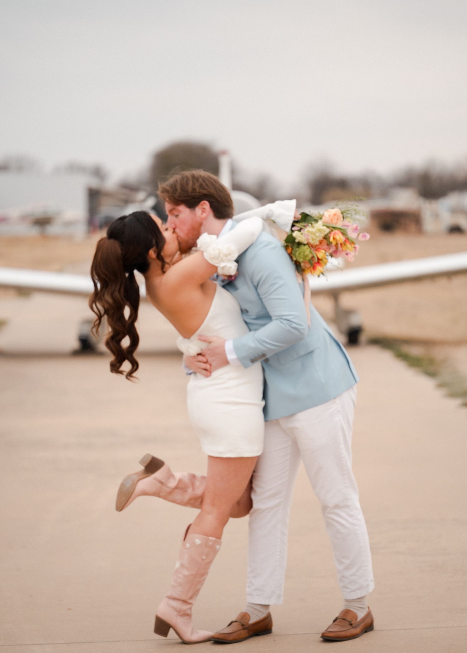 A couple in wedding attire share a romantic dip kiss on a airline strip beach at sunset. Knot & Wing Photography, Engagement photo Session