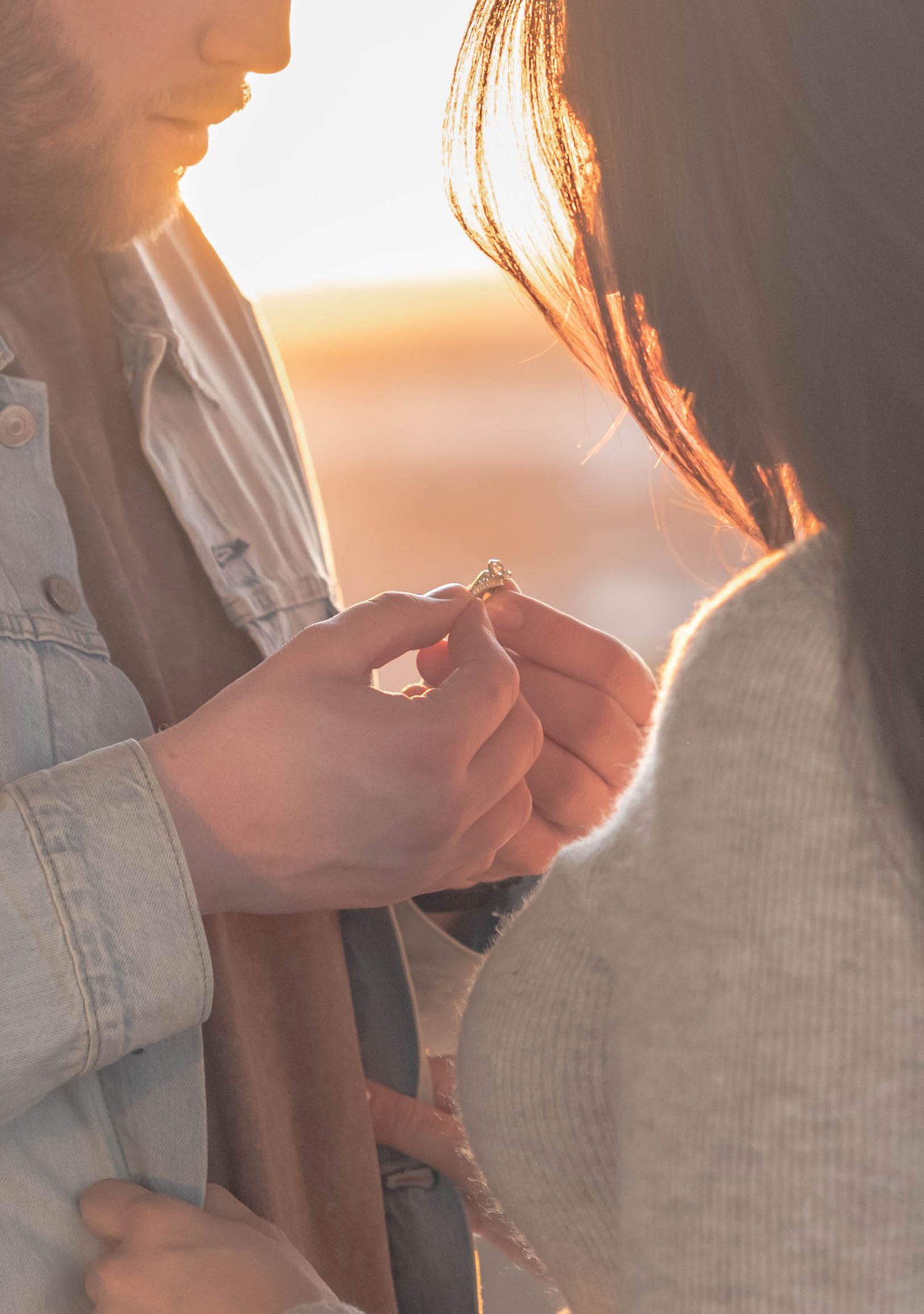 A person wearing a denim jacket holds a small object against a warm sunset background with soft lighting.