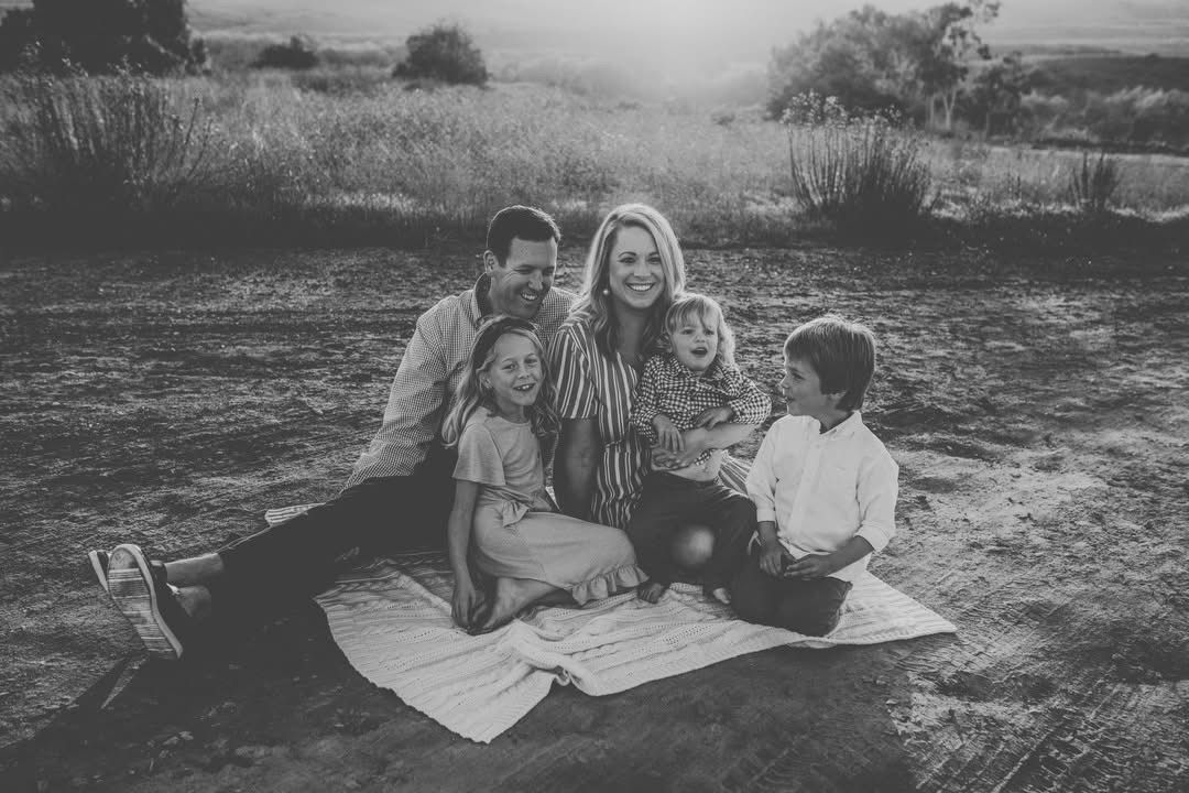 Group picnic scene on a blanket in a field with mountains visible in the distance.