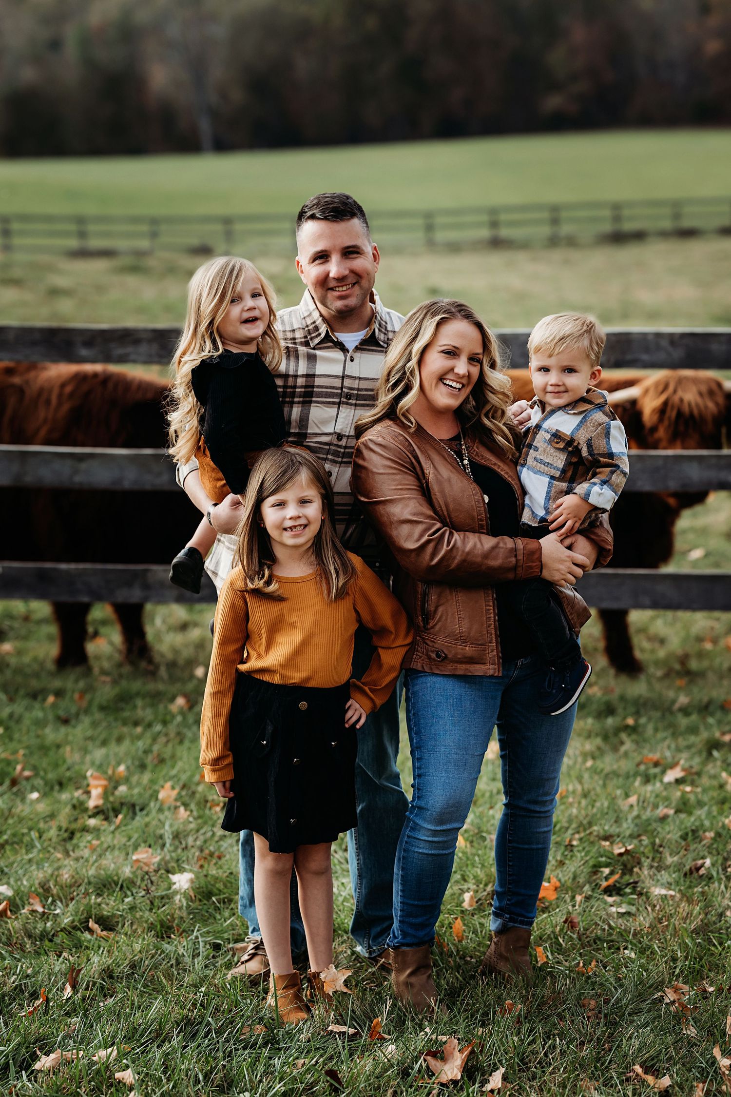 Casual outdoor family photoshoot near a rustic wooden fence with autumn foliage.