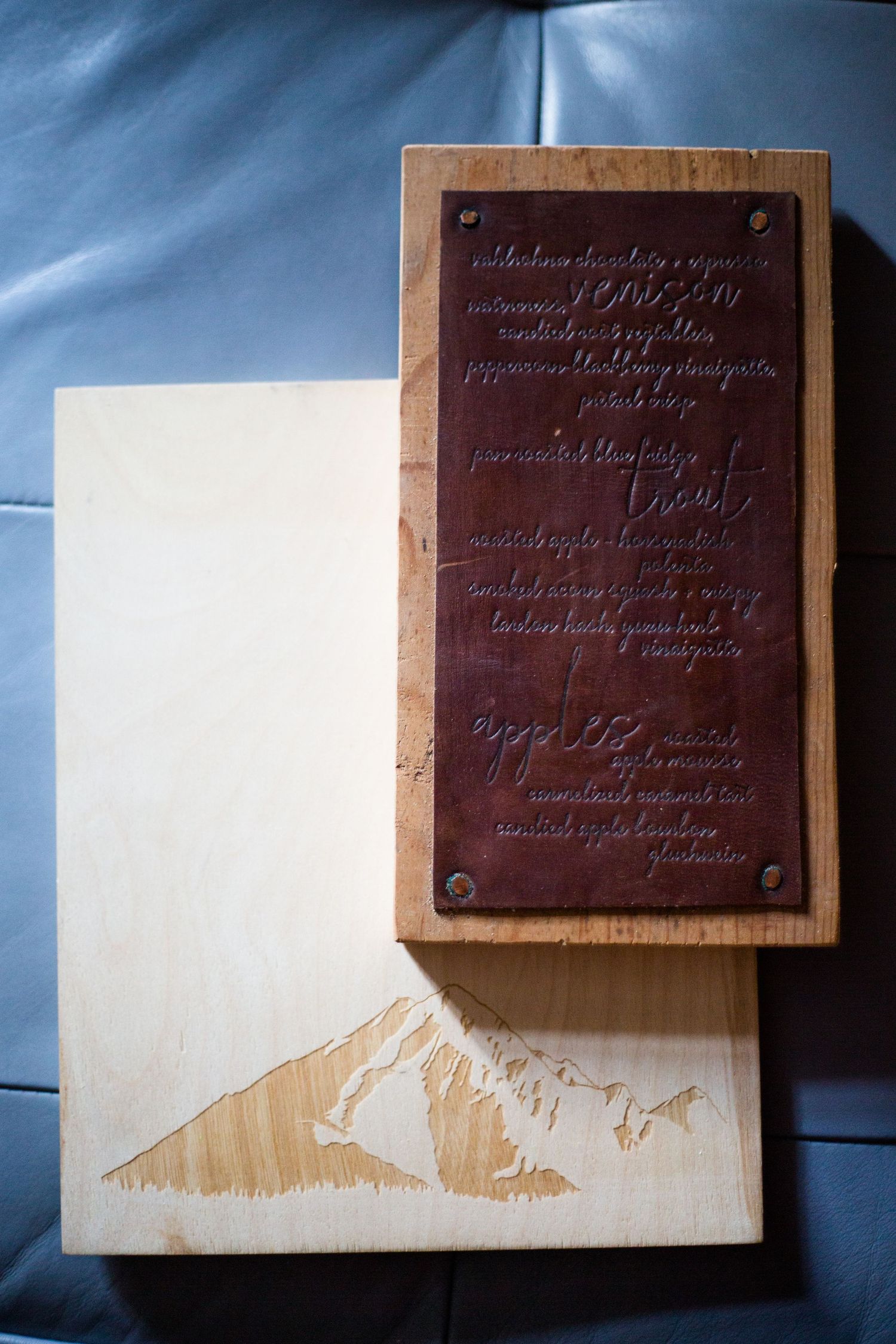 A wooden plaque with engraved copper text mounted on a light-colored board with a mountain silhouette etching.
