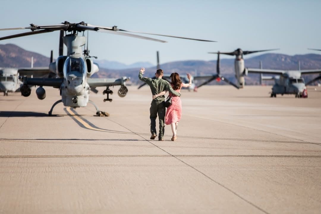 Military helicopters and aircraft lined up on a desert airfield with mountains in background.