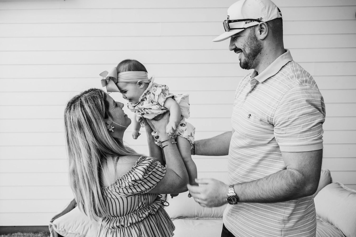 Black and white photo of parents lovingly holding their newborn baby together outdoors.