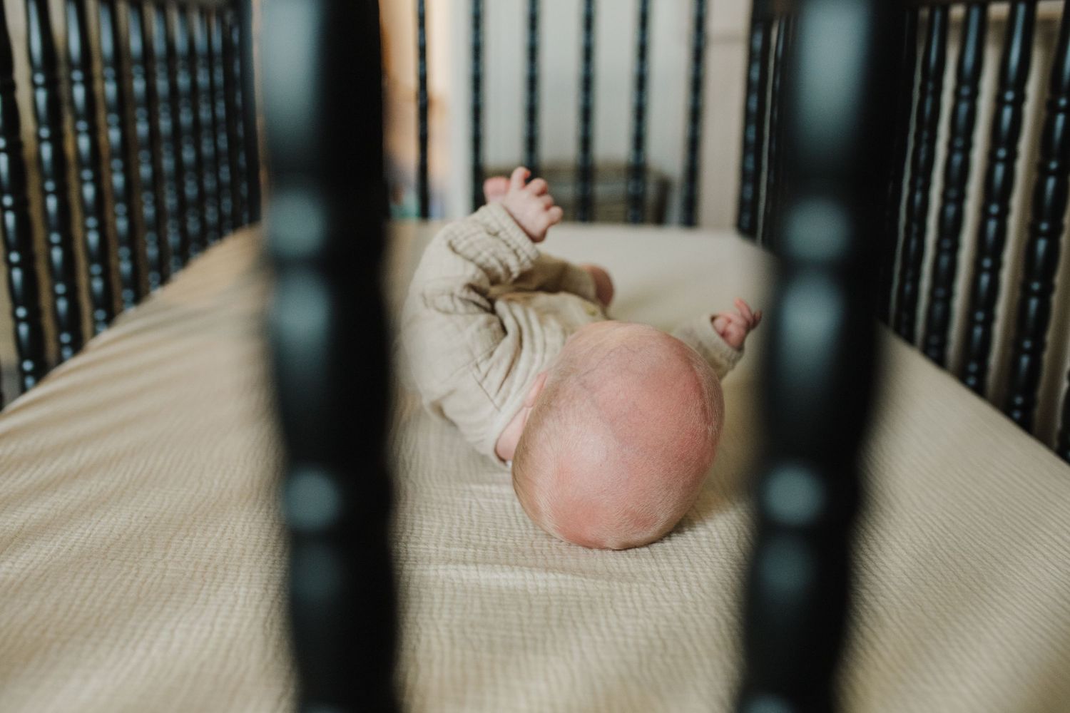 A small baby's foot is visible through the slats of a dark wooden crib.