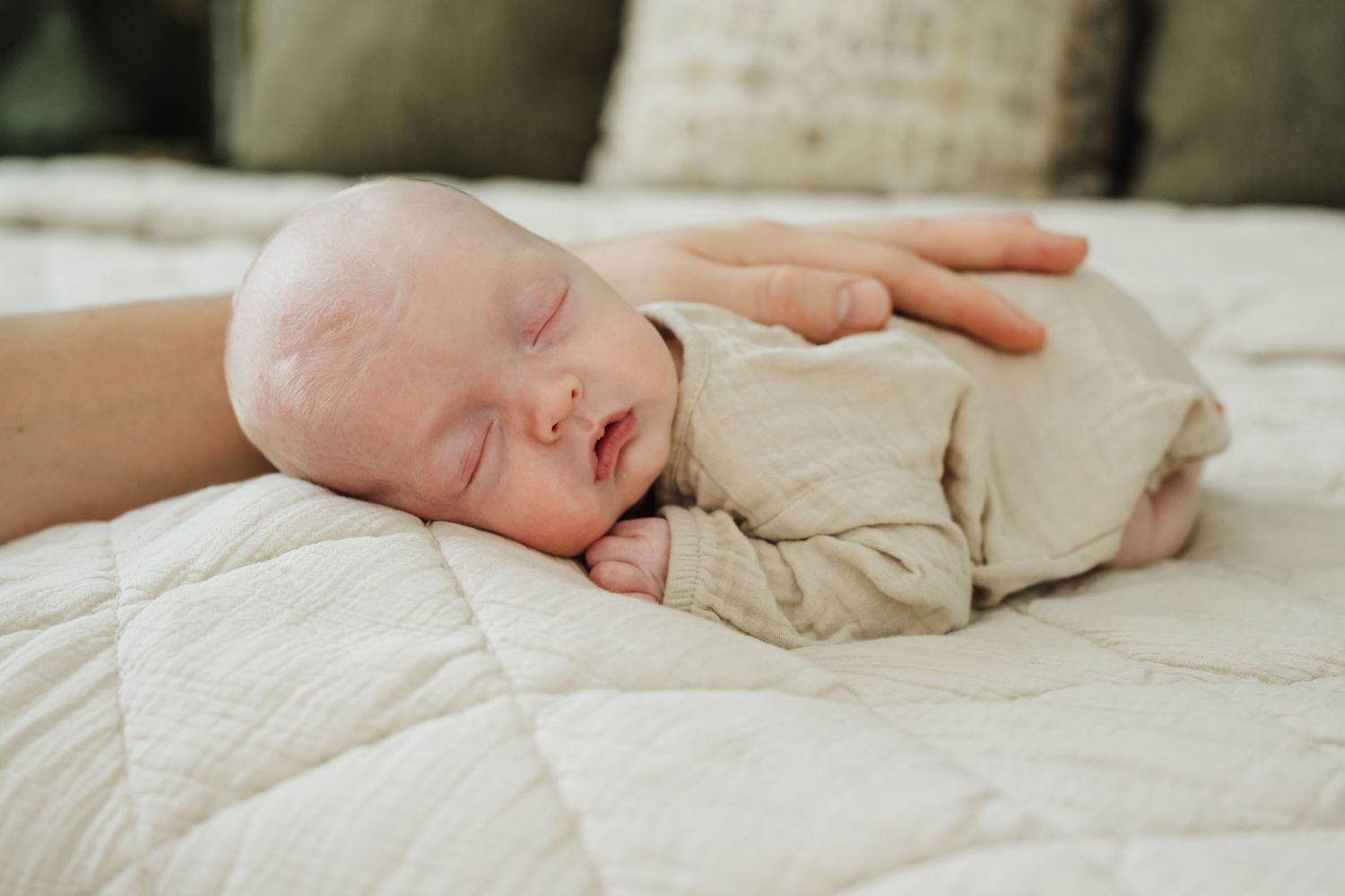 Newborn baby's tiny hand rests gently on soft white bedding, creating a tender and intimate moment.