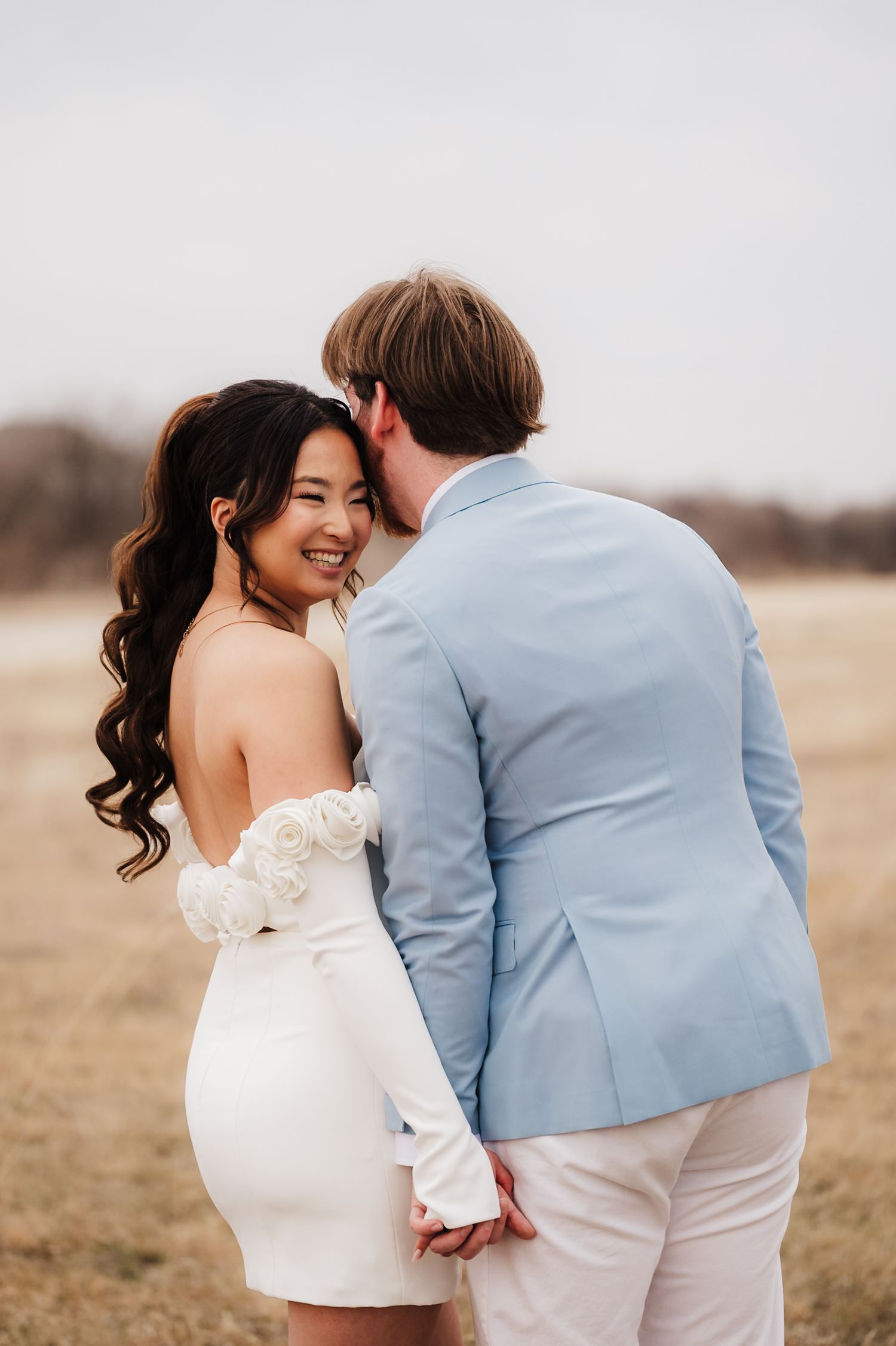 A couple in wedding attire share an intimate moment in a golden field during sunset.